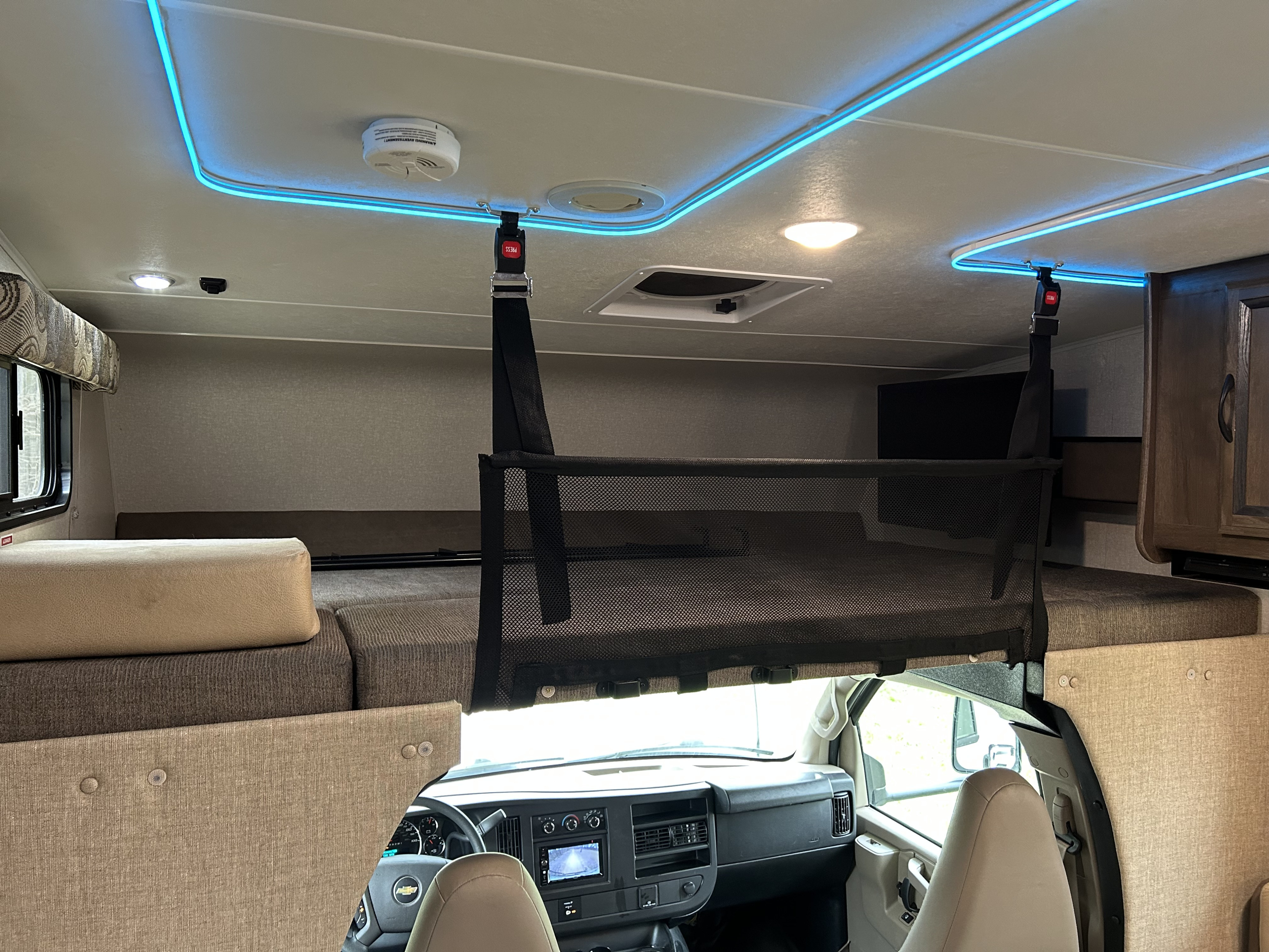 RV rental interior: cozy cab-over bunk with safety net, modern blue lighting, and view of the dashboard.. Coachman Freelander 26DS 2019