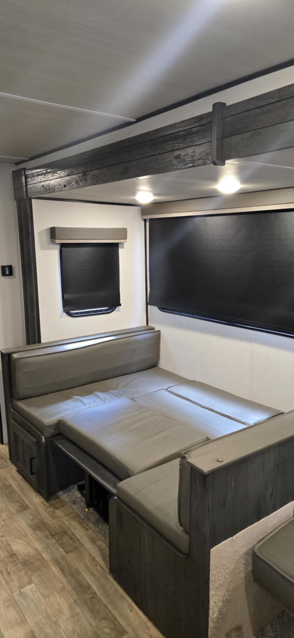 Cozy RV rental interior features a grey dinette converted into a comfortable bed with dark blinds & ceiling lights.. Keystone Hideout 2022