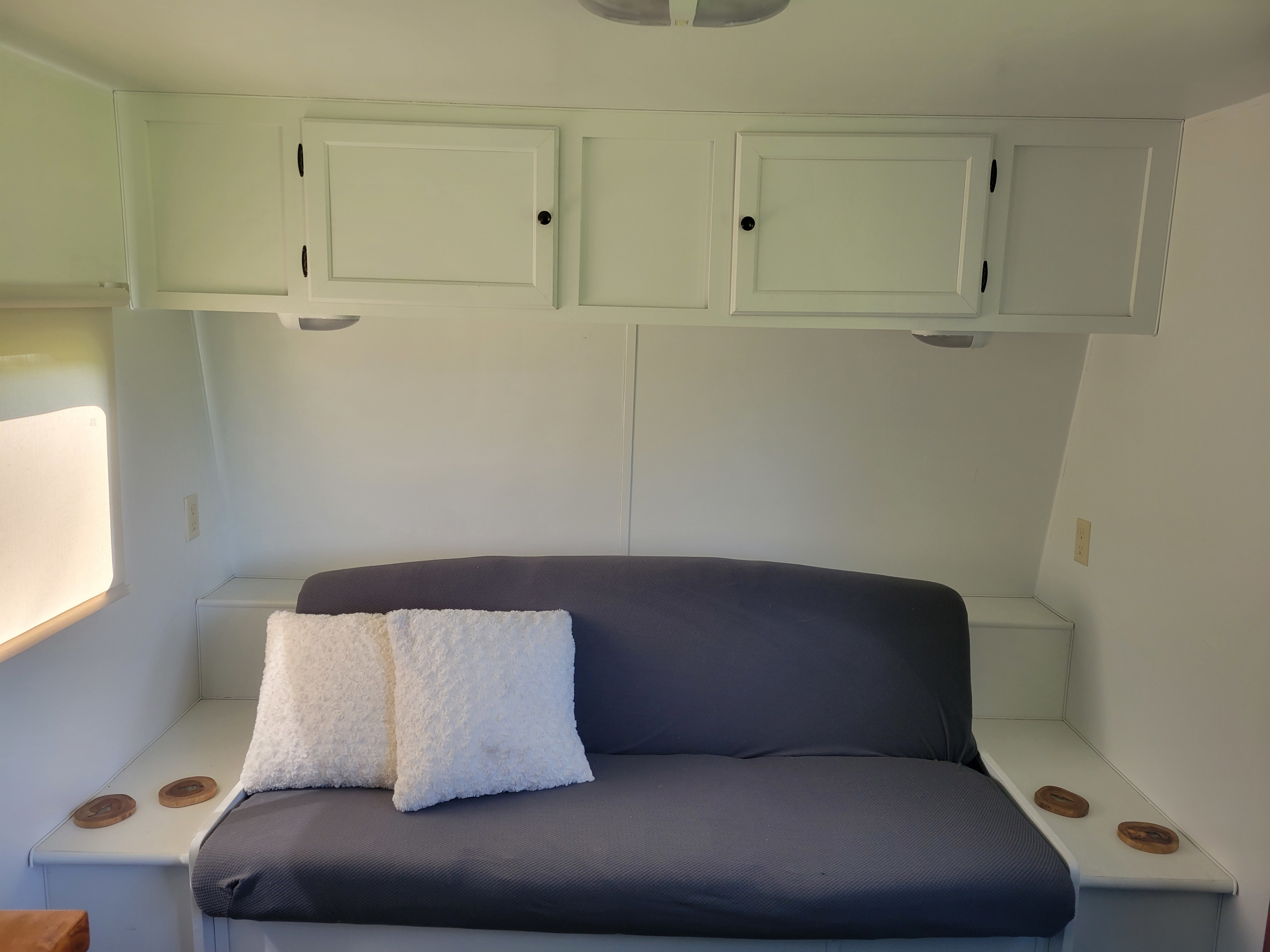 Bright RV rental interior with a dark grey sofa, convenient side shelves, and white overhead storage cabinets.. Dutchmen Weekender 2010