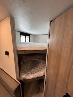 Step inside this rv rental to find convenient bunk beds, featuring cozy white bedding and a window above the top bunk.. Keystone RV Coleman 23B 2025