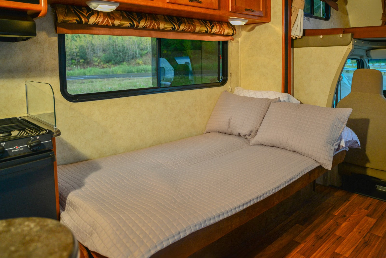 Compact RV rental interior featuring a cozy bed, small kitchen, and window view for comfortable travel.. Forest River Coachmen Freelander 2014