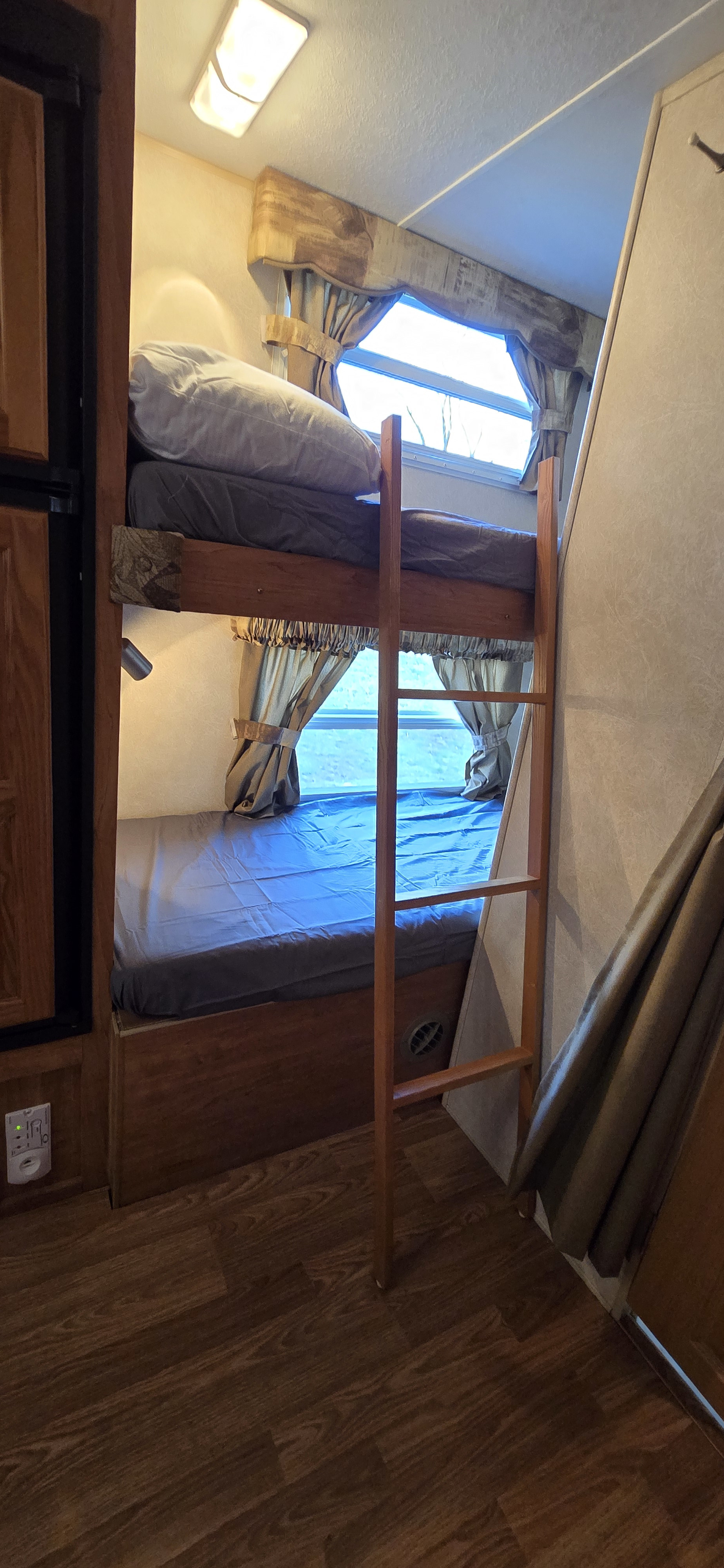 Inside an RV rental, showing cozy bunk beds with a wooden ladder, window with curtains, and warm lighting.. Forest River Flagstaff Super Lite 2008