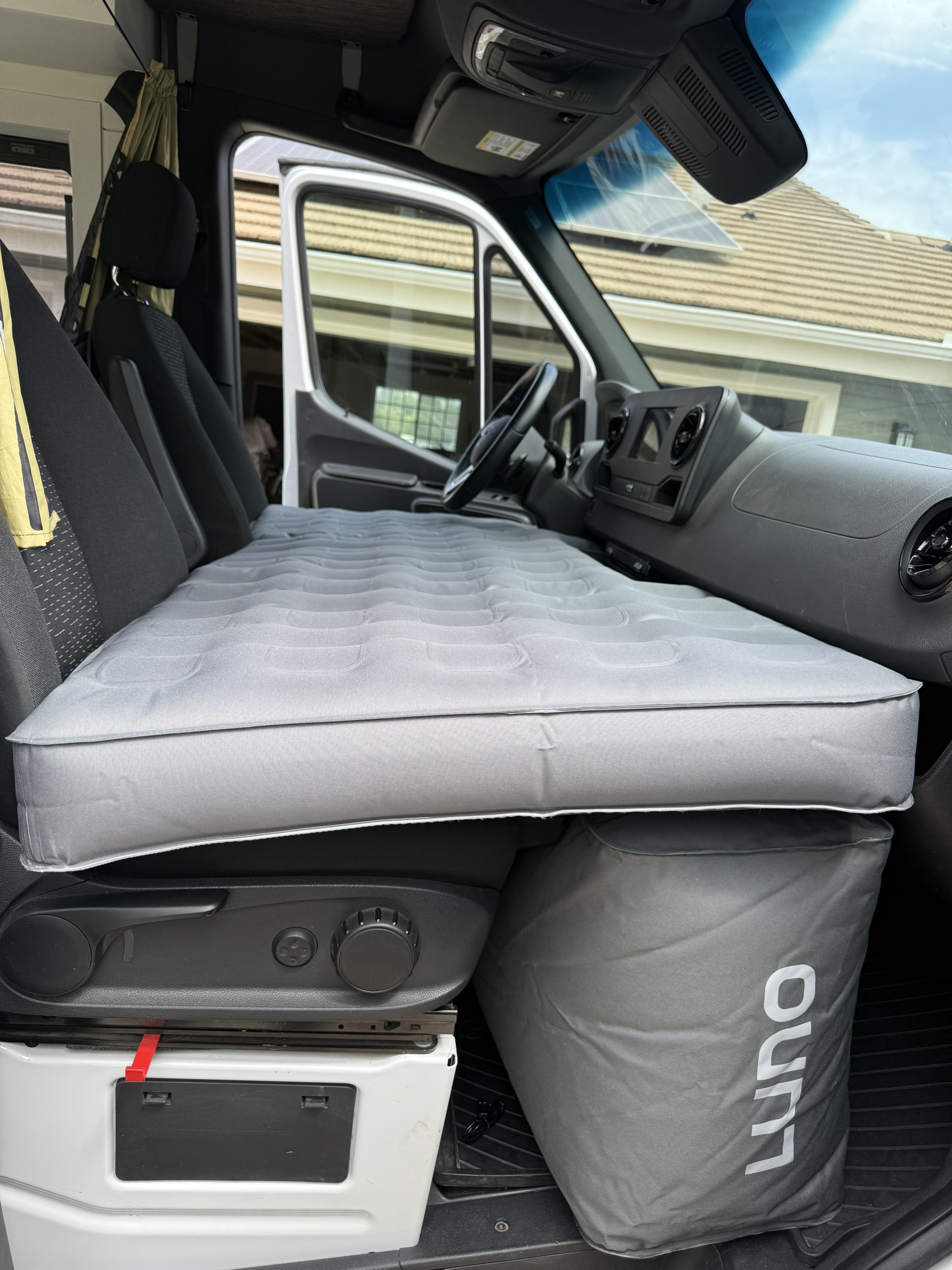 Inside an RV rental, a grey Luno air mattress spans the front seats, converting the cabin into a comfortable sleeping area.. Mercedez-Benz Sprinter 2021