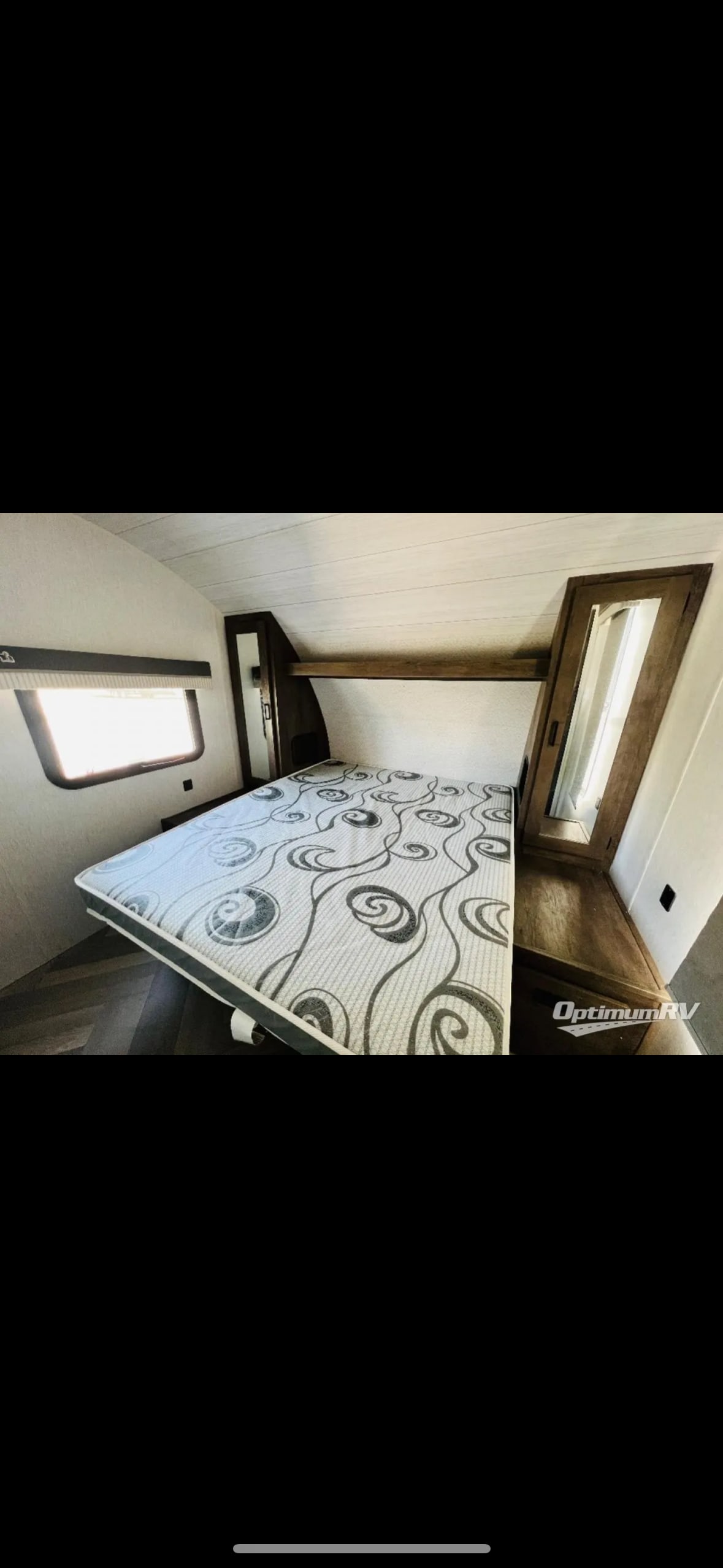 RV rental bedroom featuring a patterned mattress, window, and wood accents. Perfect for cozy adventures.. Forest River Wildwood X-Lite 2022