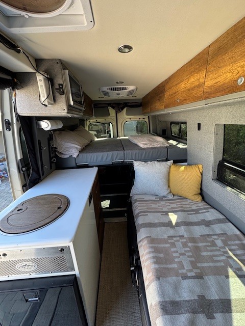 Inside an RV rental: a cozy camper van interior with a galley, elevated rear bed, and side bench/bed.. Storyteller Overland Beast 2023