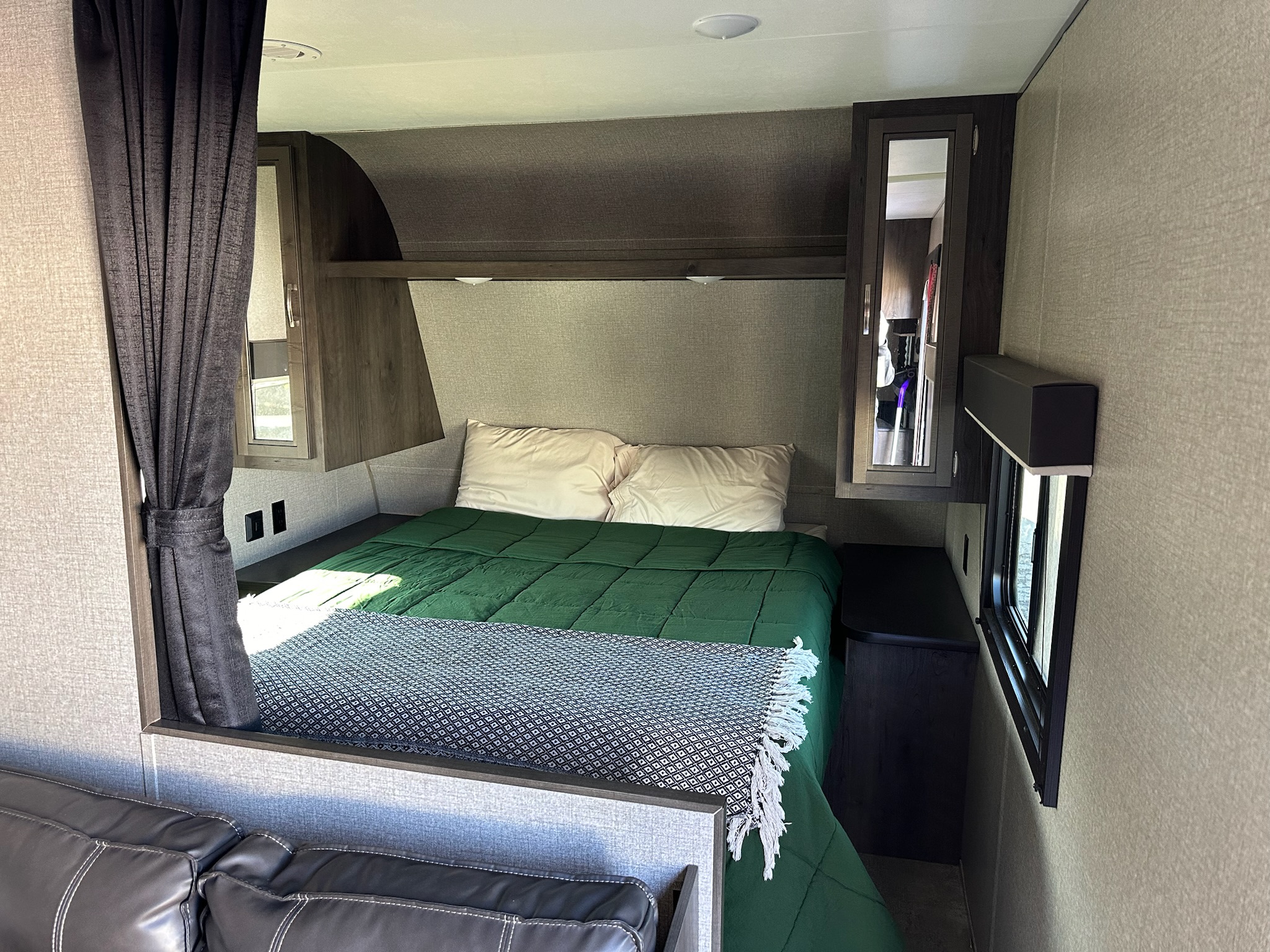 Cozy RV rental bedroom with a green comforter, white pillows, dark wood cabinets, and a privacy curtain. Compact and functional.. Jayco Jay Flight SLX 2021