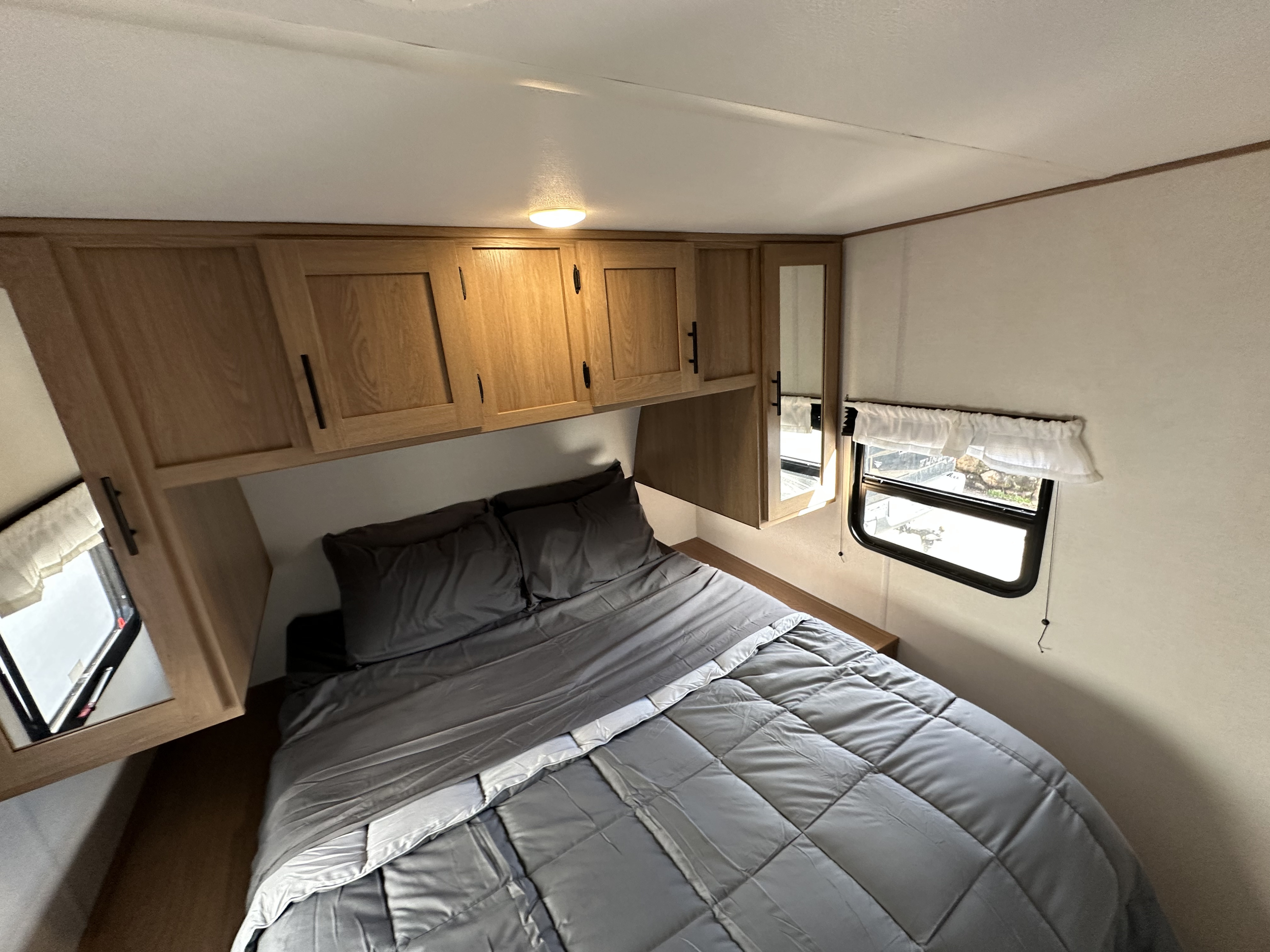 Interior of an RV rental bedroom featuring a bed with gray bedding, wooden overhead cabinets, and a window.. Fmc Primetime 2022