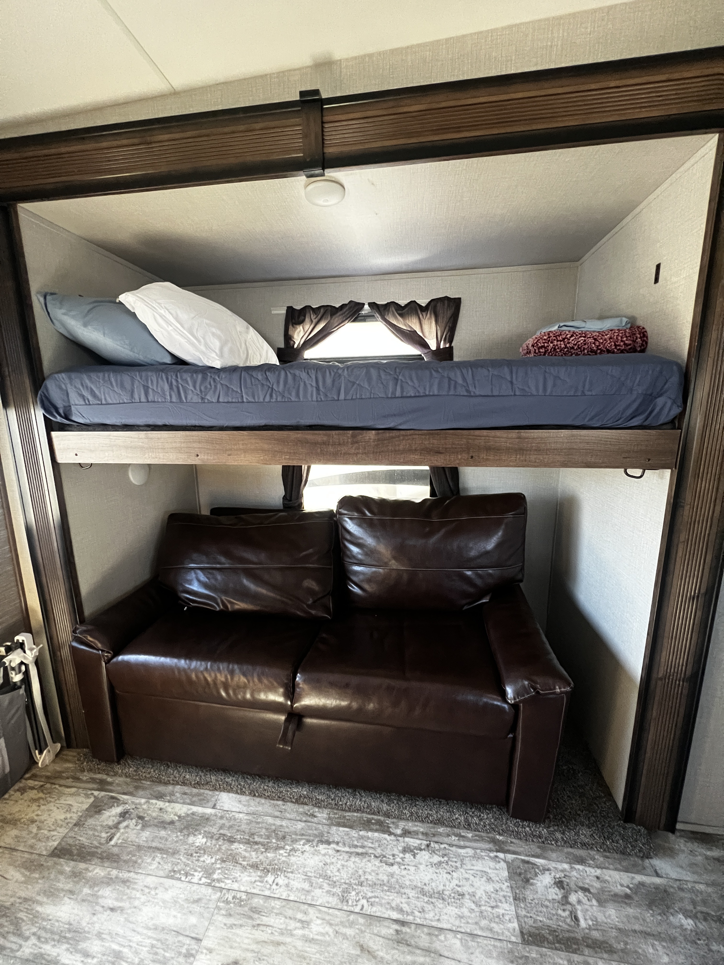 RV rental bunk area: a comfortable top bunk with blue bedding positioned above a brown leather sofa.. K-Z Manufacturing Durango 2020