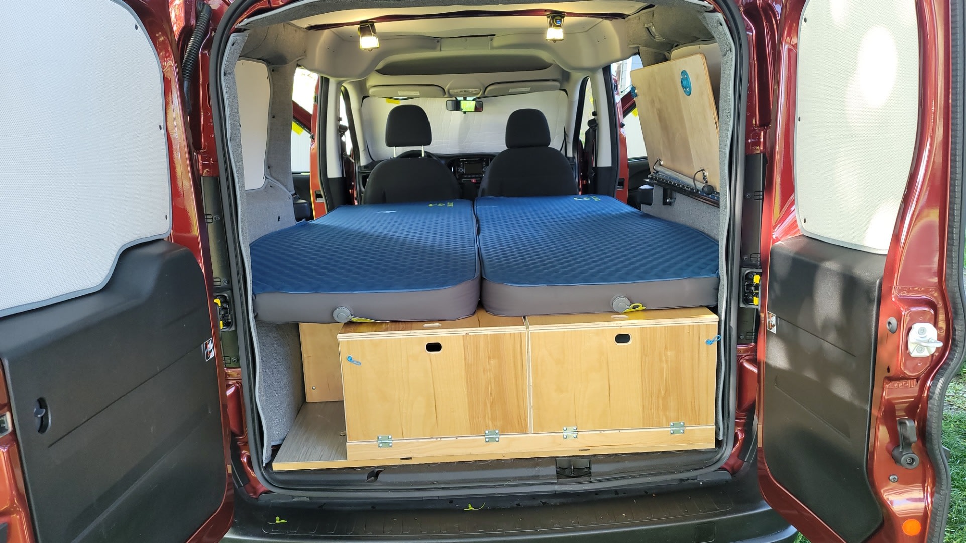 RV rental: Camper van interior from rear, featuring two blue inflatable beds over wooden storage drawers.. RAM Promaster CIty 2018