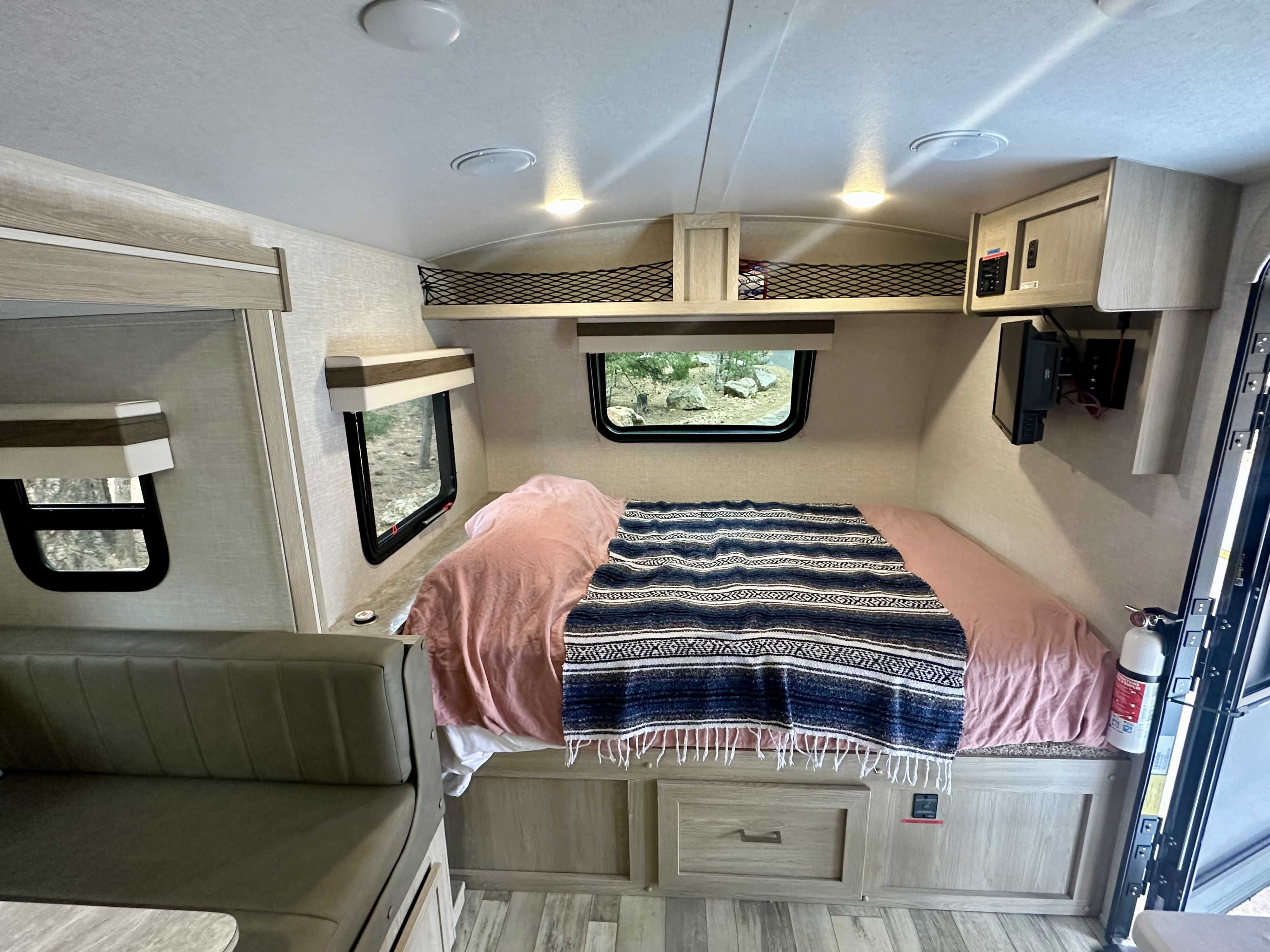Interior view of an RV rental, showing a cozy bed, windows with a natural view, and a small living area in a camper.. Rockwood Geo Pro 2022