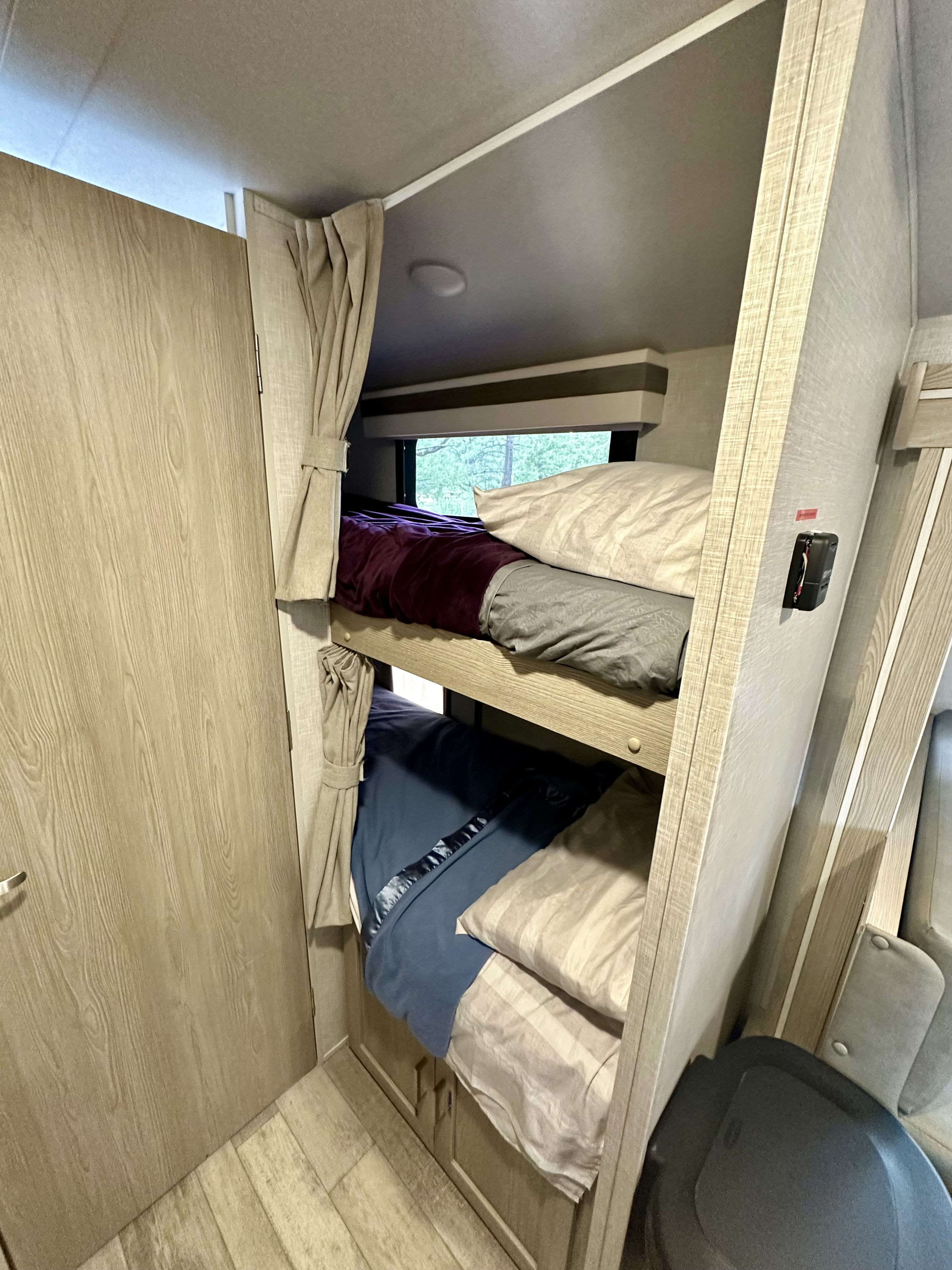 Cozy RV rental interior featuring two comfortable bunk beds with bedding, a window with a treeline view, and a wooden door.. Rockwood Geo Pro 2022