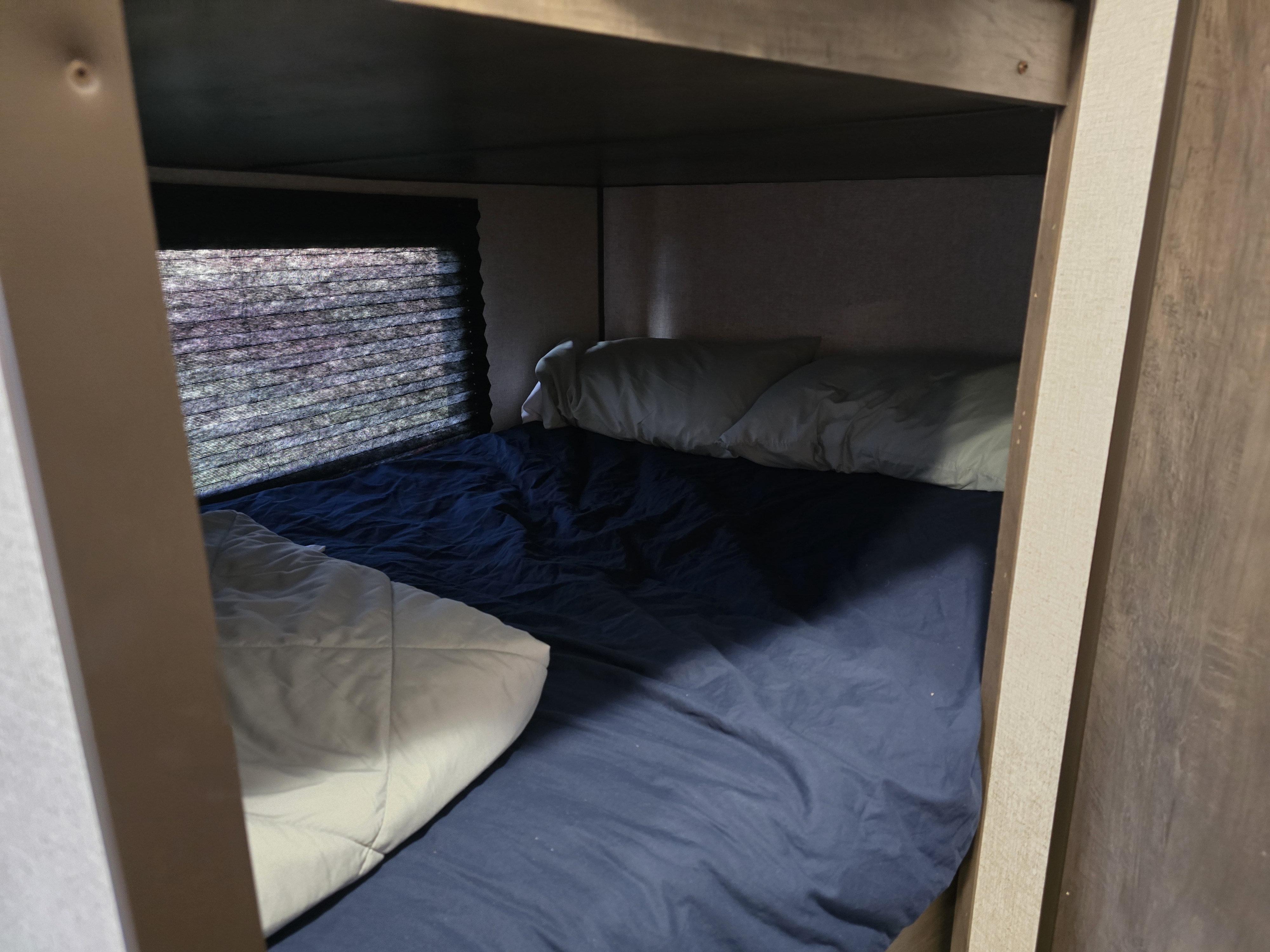 Cozy bunk bed with blue sheets, white pillows, and window blinds inside an RV rental, offering comfortable sleeping space.. Dutchmen Coleman Lantern 2020