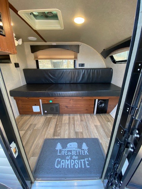 Step inside this inviting RV rental interior: a comfy bench bed, wood-look flooring, and a fun "Campsite" mat welcome you.. Sunset Park RV SunRay 2019