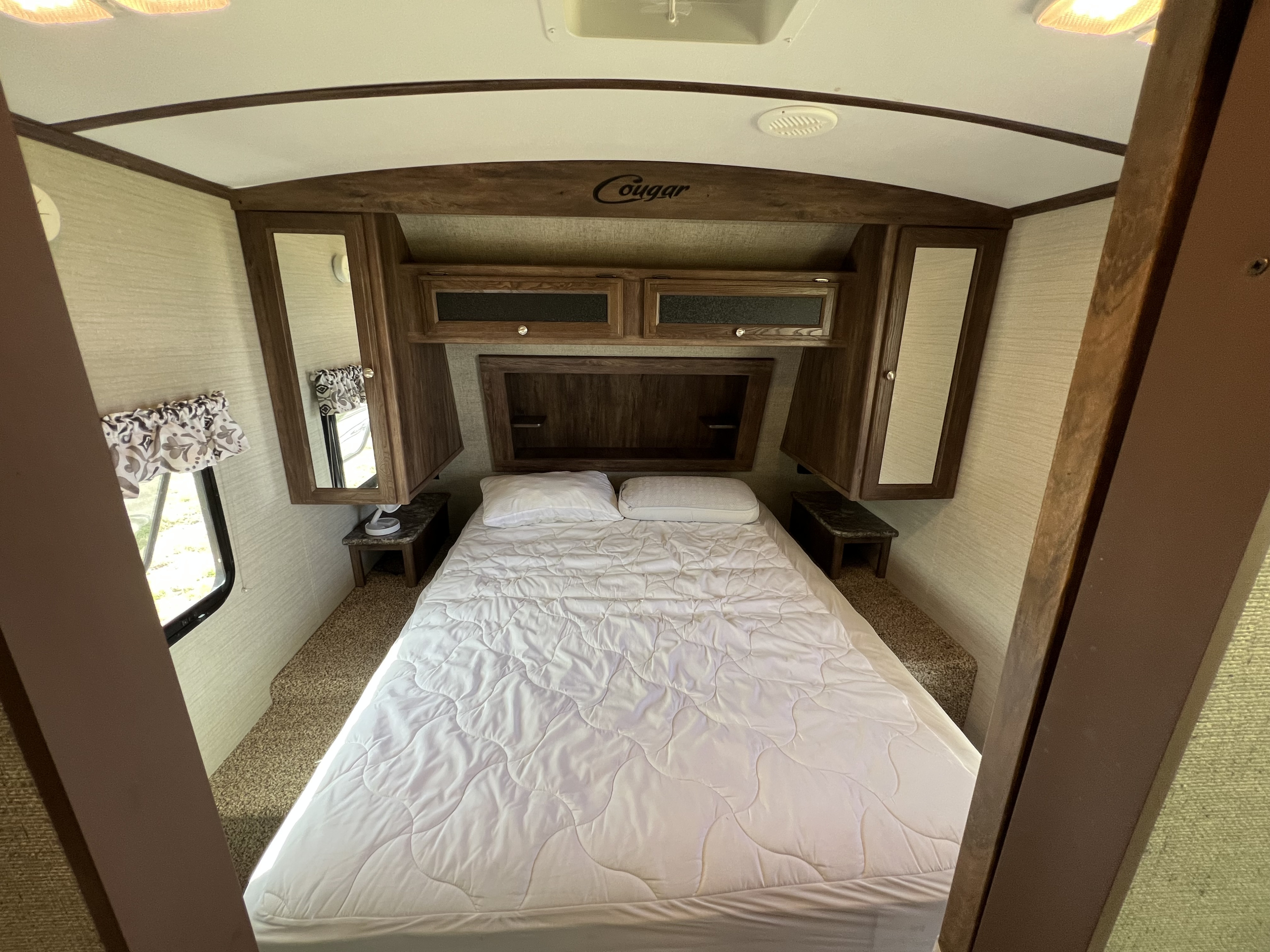 Spacious queen bedroom in an RV rental, featuring overhead storage, a window, and comfortable white bedding.. Keystone RV Cougar 2017