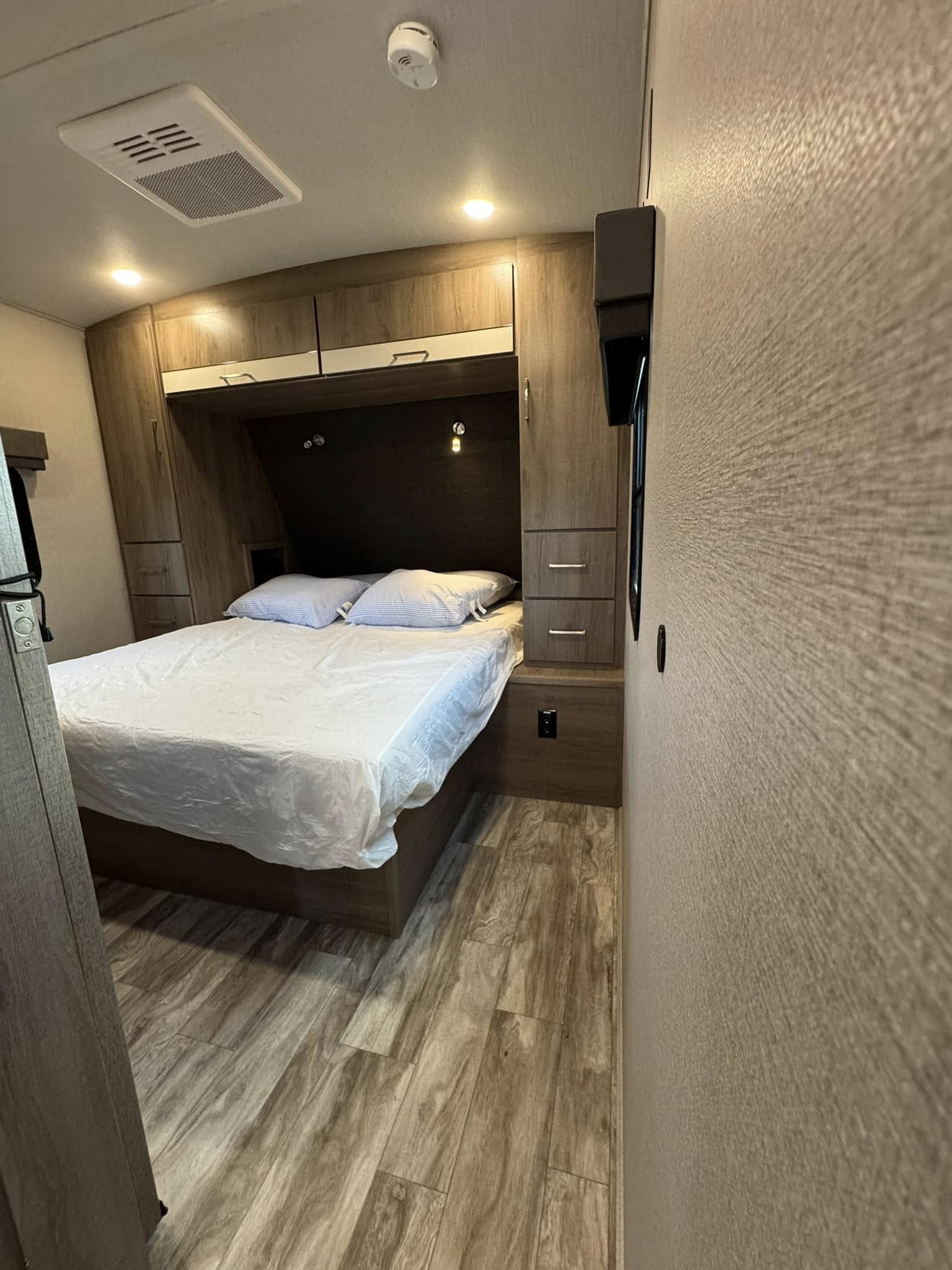 Inside an RV rental: a cozy bedroom featuring a bed with white linen, built-in storage, and wood-look flooring.. Grand Design Imagine 2022