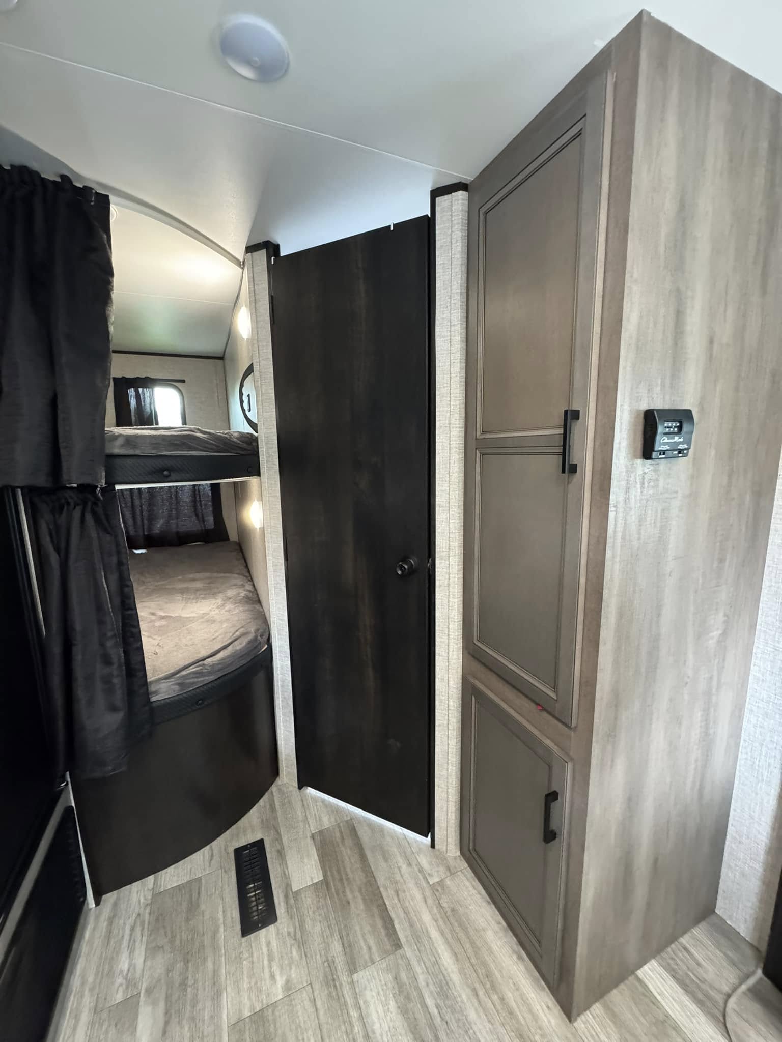 RV rental interior showcasing space-saving bunk beds with privacy curtains, a central door, and a versatile storage cabinet with controls.. Jayco Jay Flight 2022