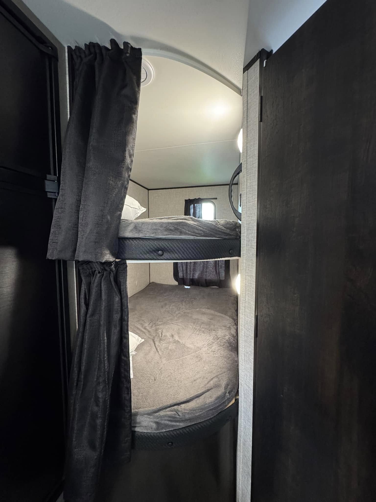 Interior view of an RV rental showing stacked bunk beds, each with dark privacy curtains and cozy gray bedding.. Jayco Jay Flight 2022