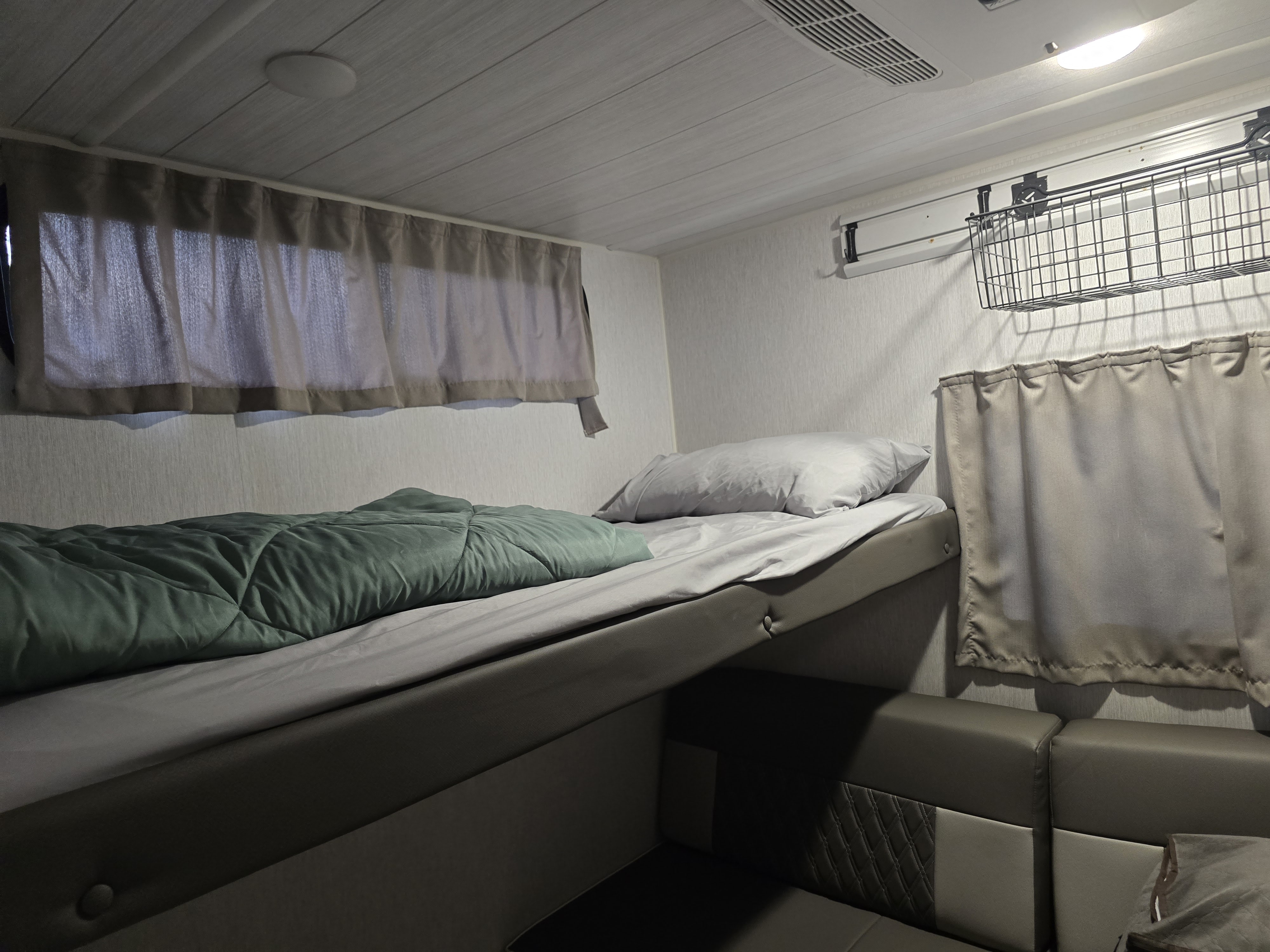 Cozy RV rental interior with a bunk bed over a sofa, dim lighting, and soft curtains for a comfortable stay.. Forest River Wildwood X-Lite Platinum 2023