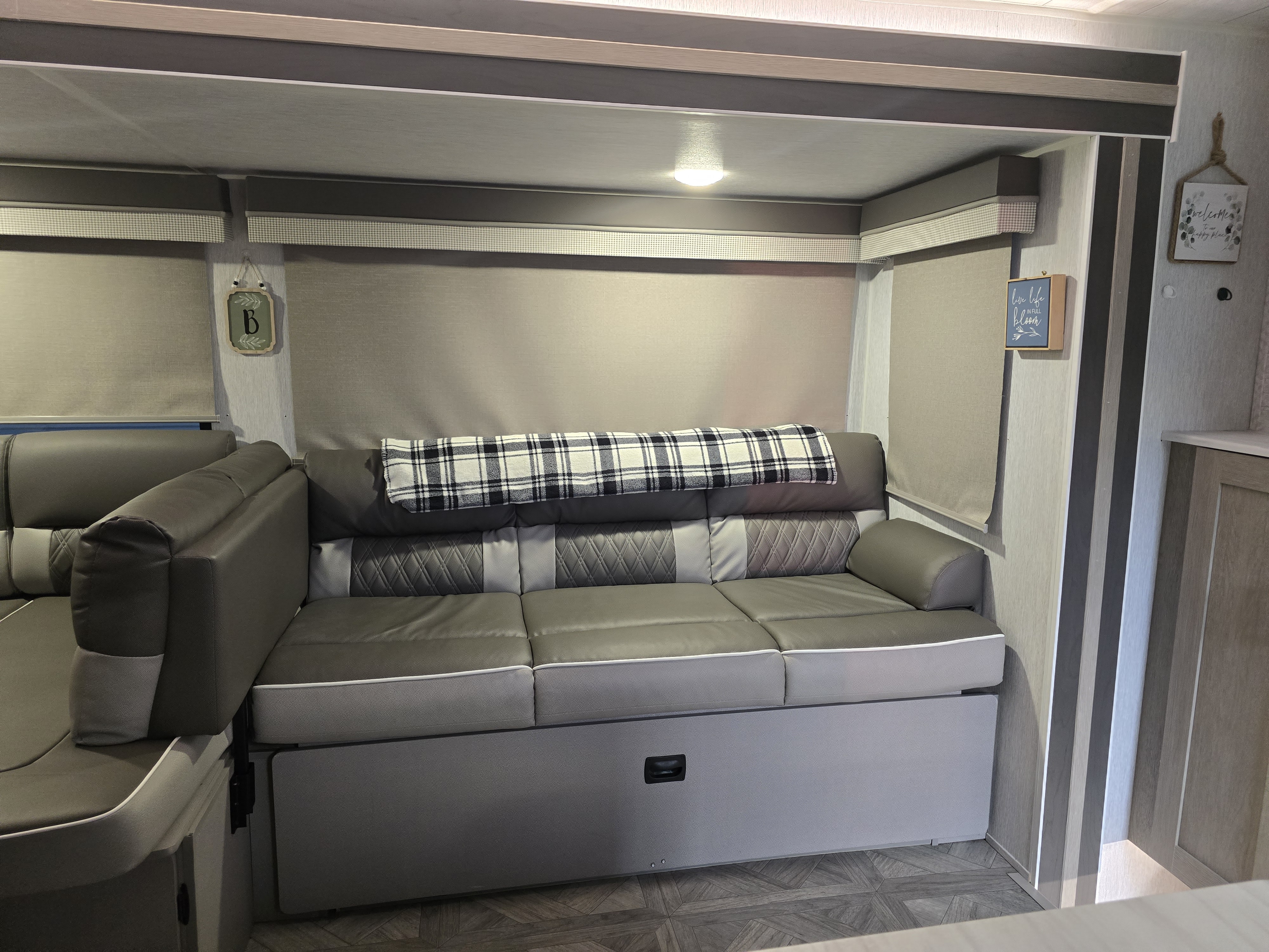 RV rental interior: comfy gray convertible sofa, plaid blanket, and sleek blinds in a neutral living space.. Forest River Wildwood X-Lite Platinum 2023