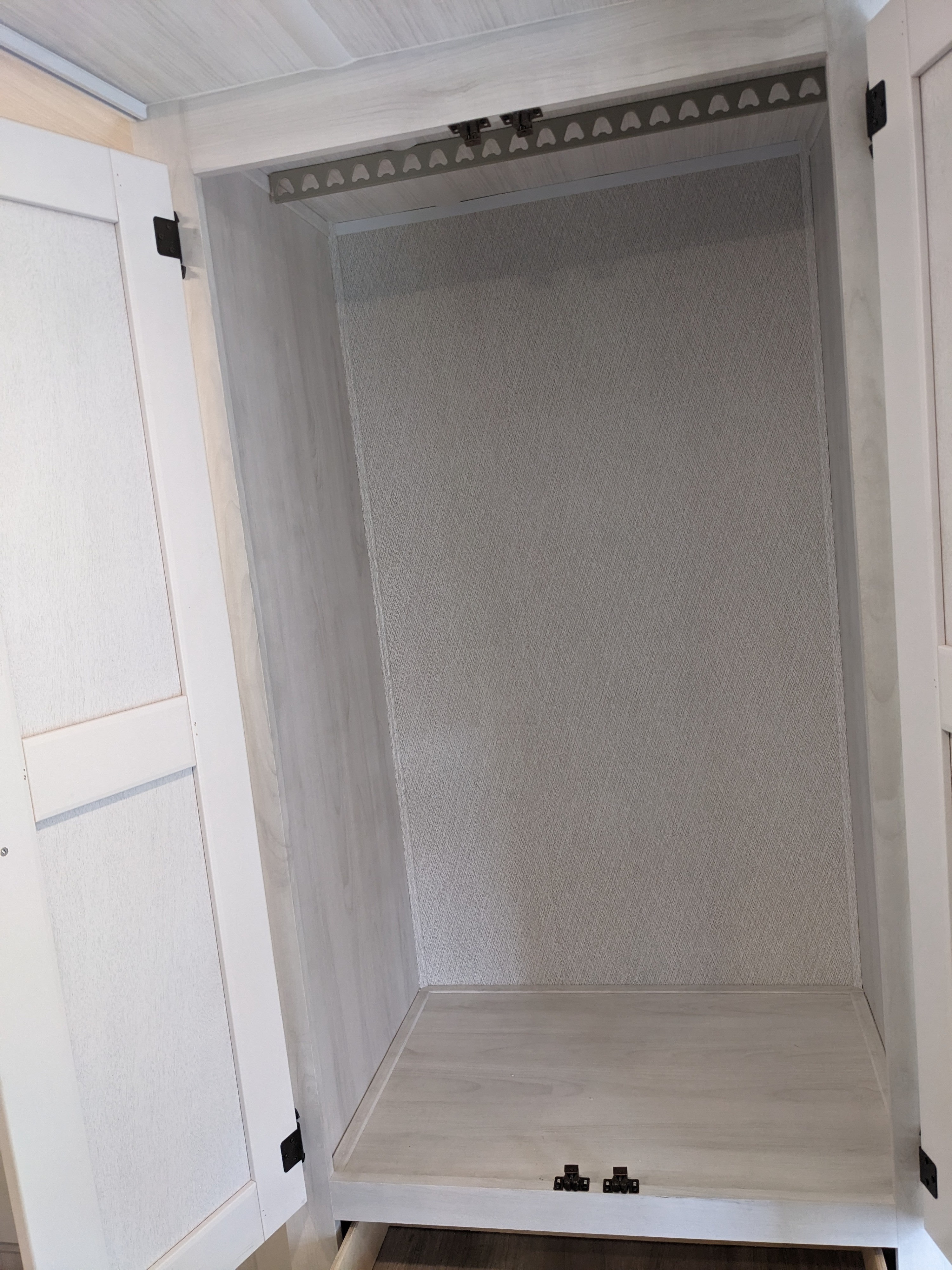Empty RV rental wardrobe features light wood, textured walls, a clothes rod, and a pull-out drawer at the base.. East to West Entrada 2026