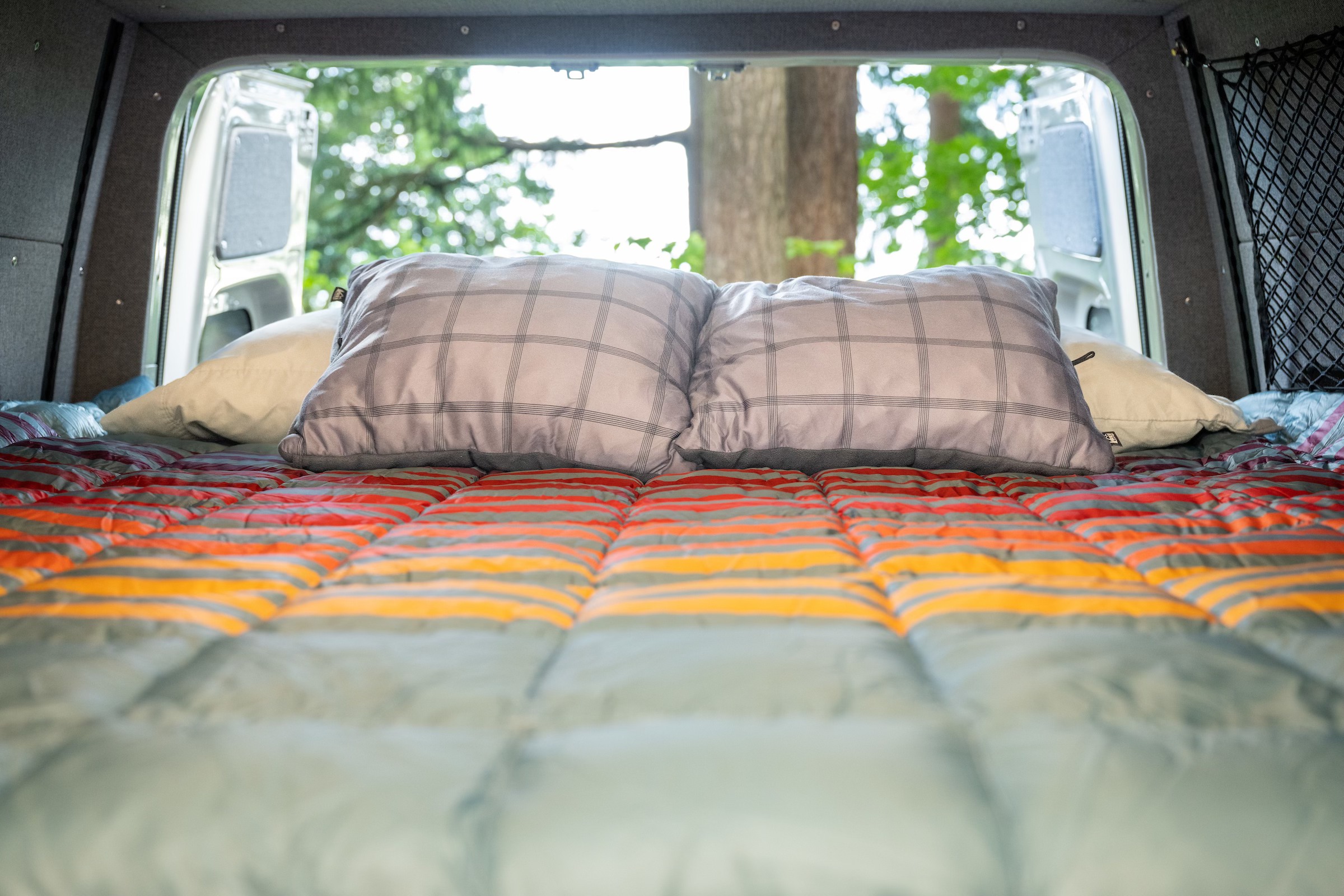 Cozy RV rental bed with open back doors revealing a natural view. Perfect for van life adventures from inside a campervan.. Mercedes-Benz Sprinter 2021