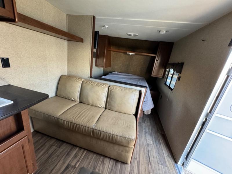 Inside an RV rental: a comfortable beige sofa, small counter with sink, and a cozy bedroom with a bed. Compact living space.. Heartland Prowler Lynx 2015