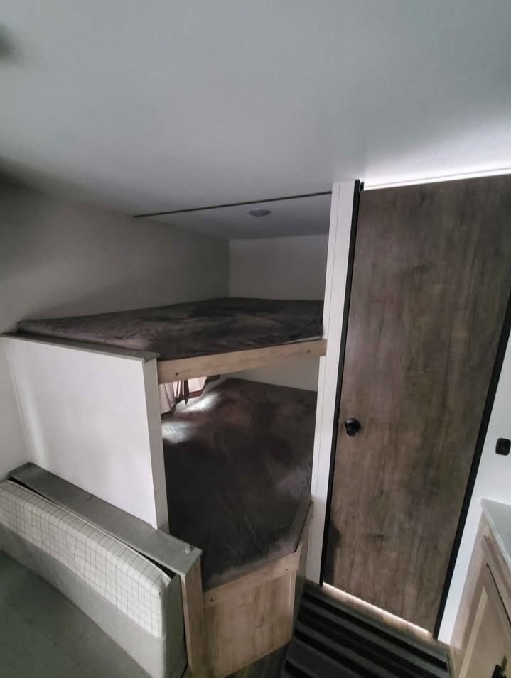 RV rental interior featuring bunk beds and a convertible dinette. A wooden door and compact design define this sleeping area.. Gulf Stream Grand River BH25 2024