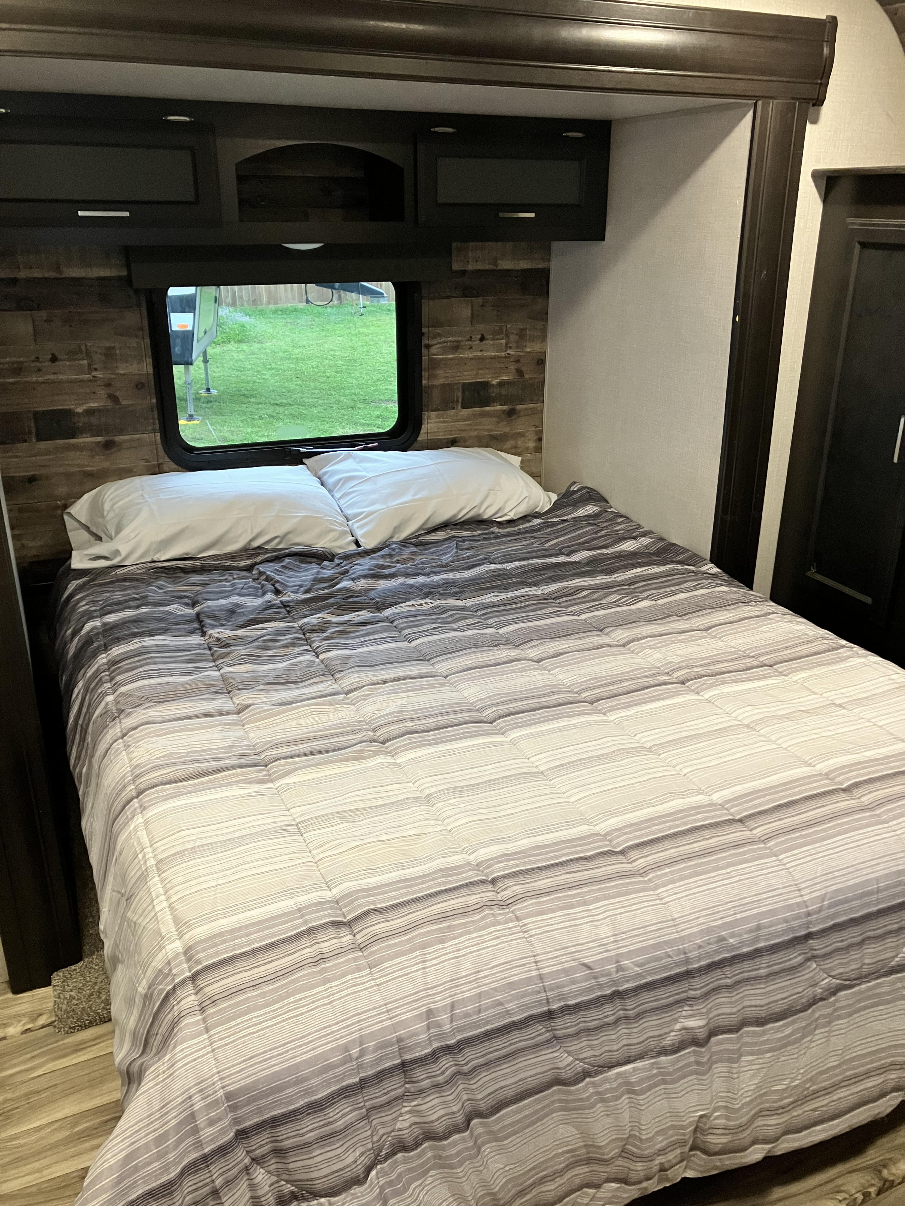 Comfortable RV rental bedroom with striped bedding, overhead cabinets, and a window view of the outdoors.. Venture SportTrek Touring 343VBH 2021