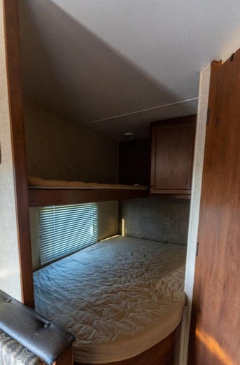 An RV rental's bunk room, featuring an upper and lower bed with a comfortable mattress, window with blinds, and cabinetry.. Heartland Prowler Lynx 2015