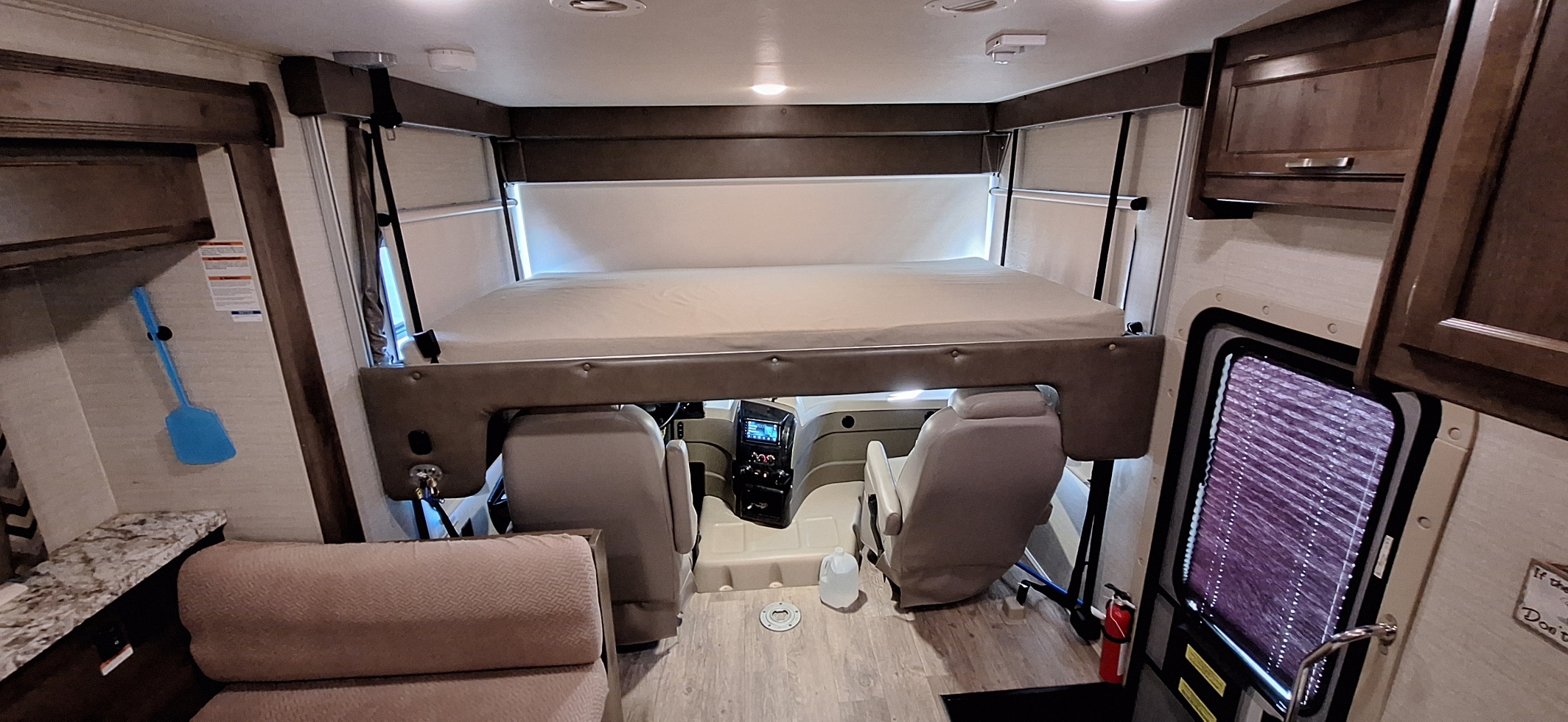 This RV rental interior shows the over-cab bunk bed, driver/passenger seats, and living area in warm tones.. Jayco Alante 2018