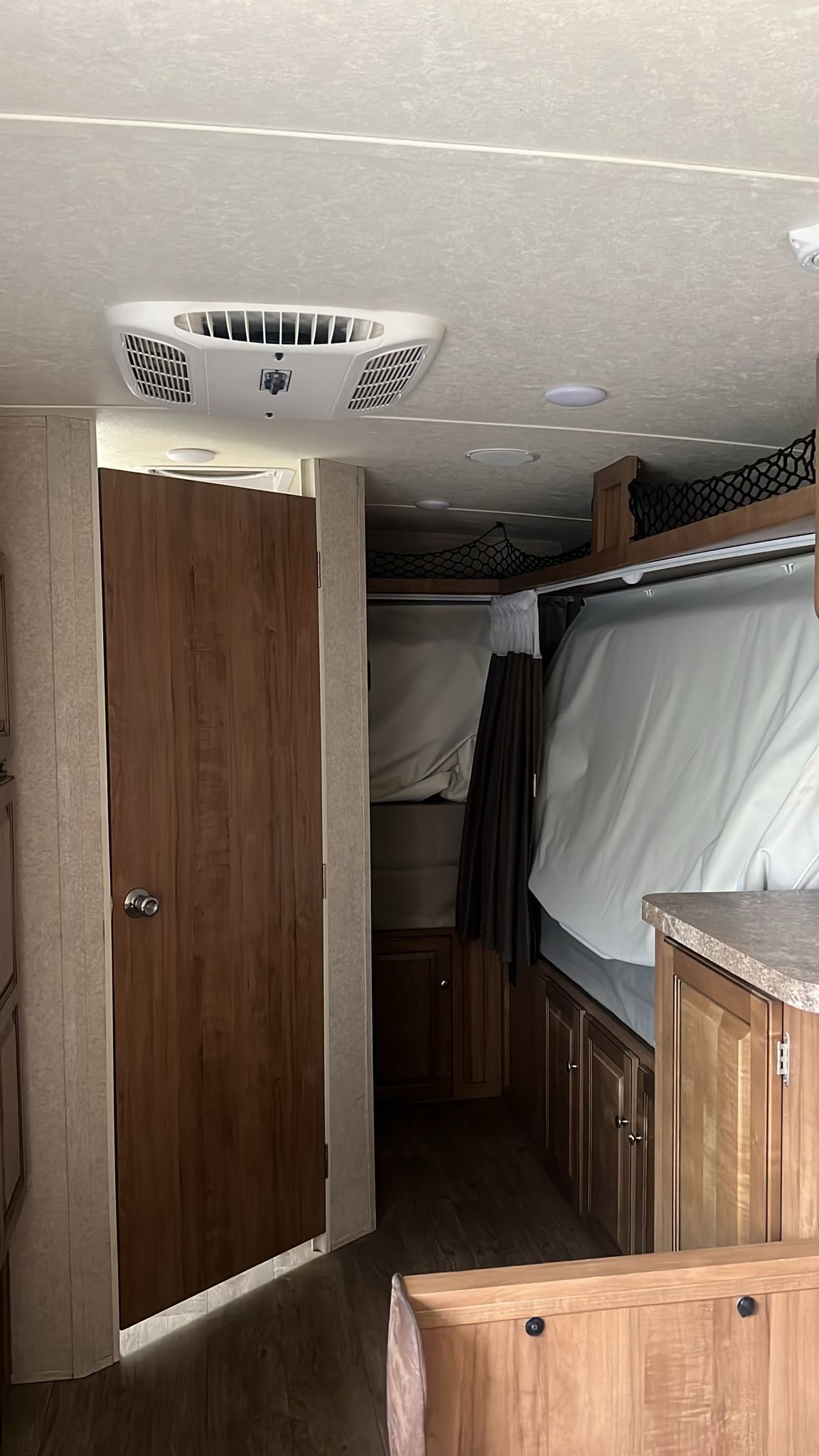 Inside an RV rental: view of bunk beds with storage nets, a white ceiling AC unit, and wood cabinetry with a door.. Forest River Rockwood Roo 2018