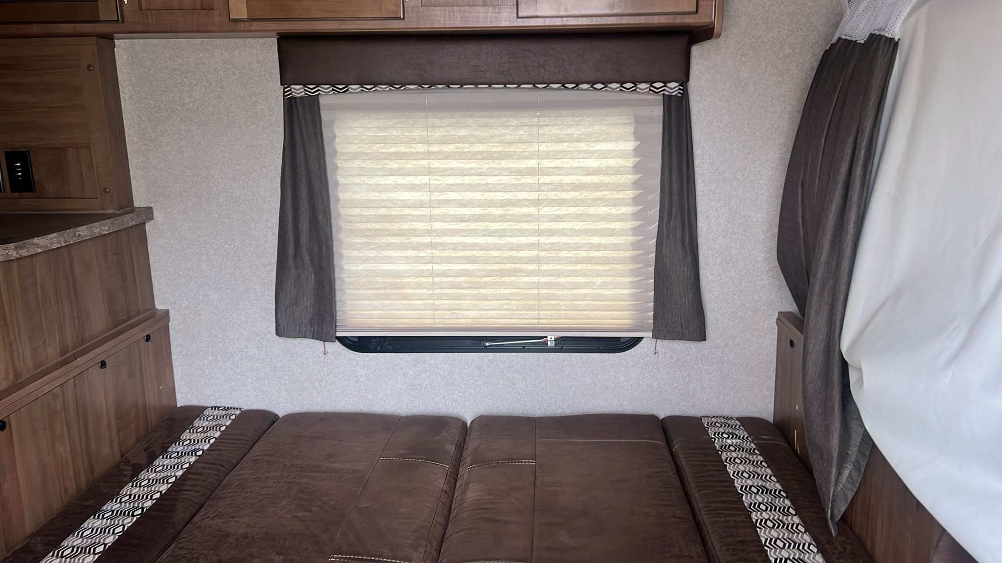 Cozy RV rental interior with a brown bed/sofa, window w/ light blinds & dark valance, plus wood cabinetry.. Forest River Rockwood Roo 2018