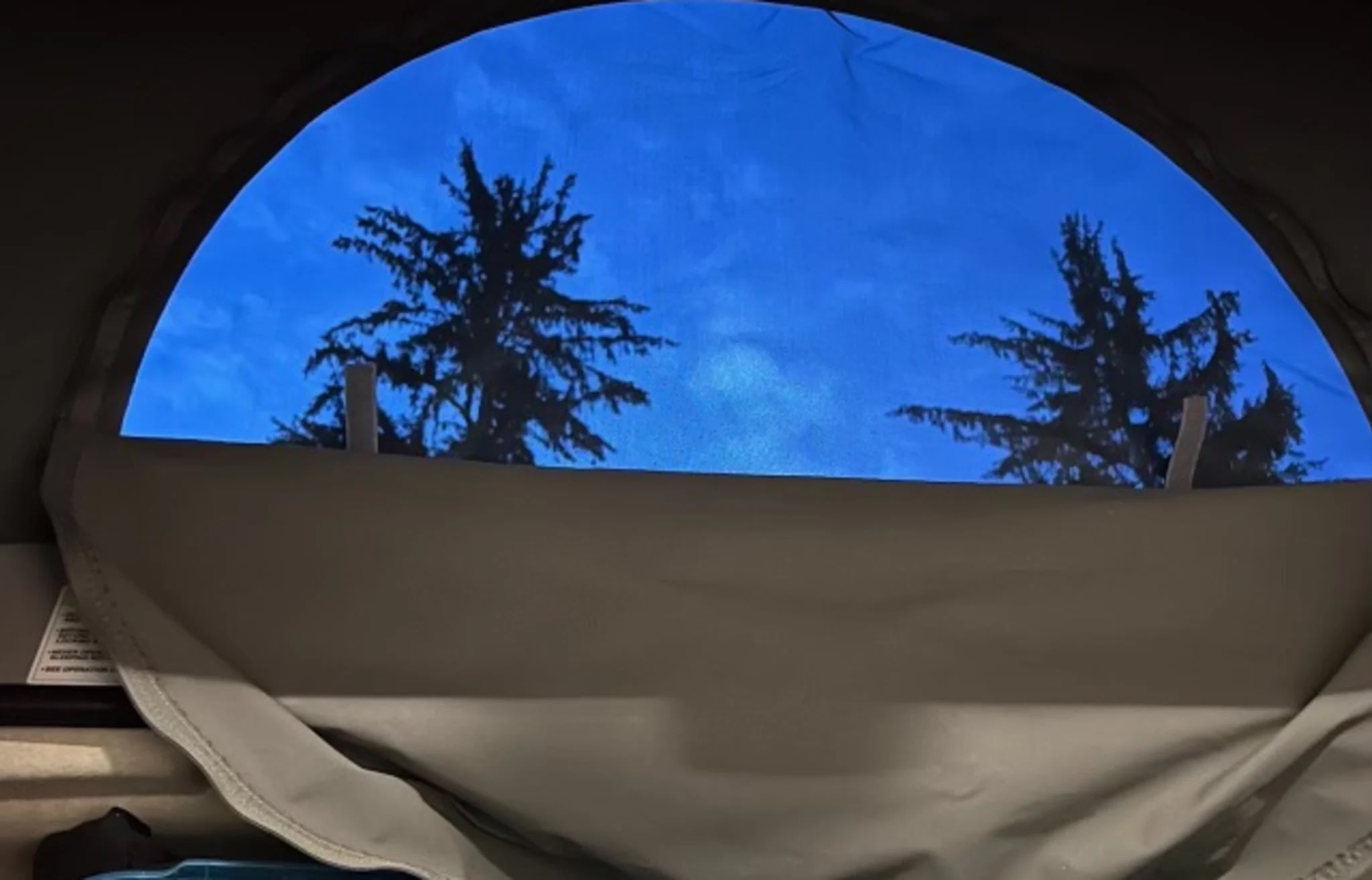 RV rental: Rounded window offers serene blue sky & silhouetted trees. Ideal for nature & camping travel.. Winnebago Solis 2023