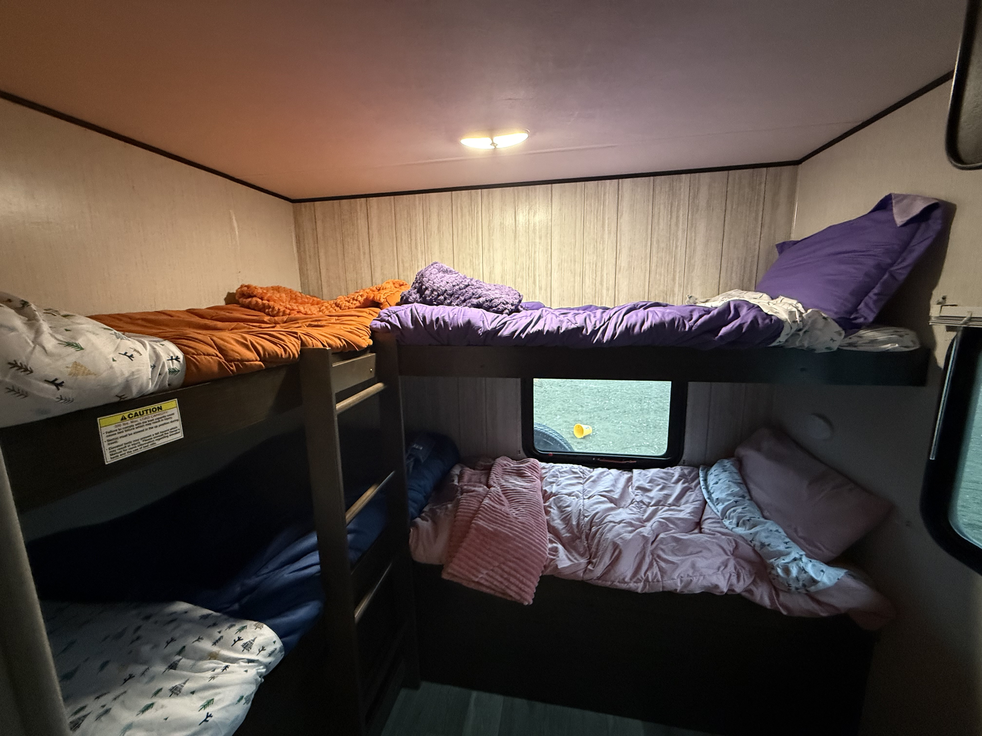 Inside an RV rental, this cozy sleeping area features multiple bunk beds with colorful bedding and a window showing outdoors.. Heartland RVs Pioneer 2022