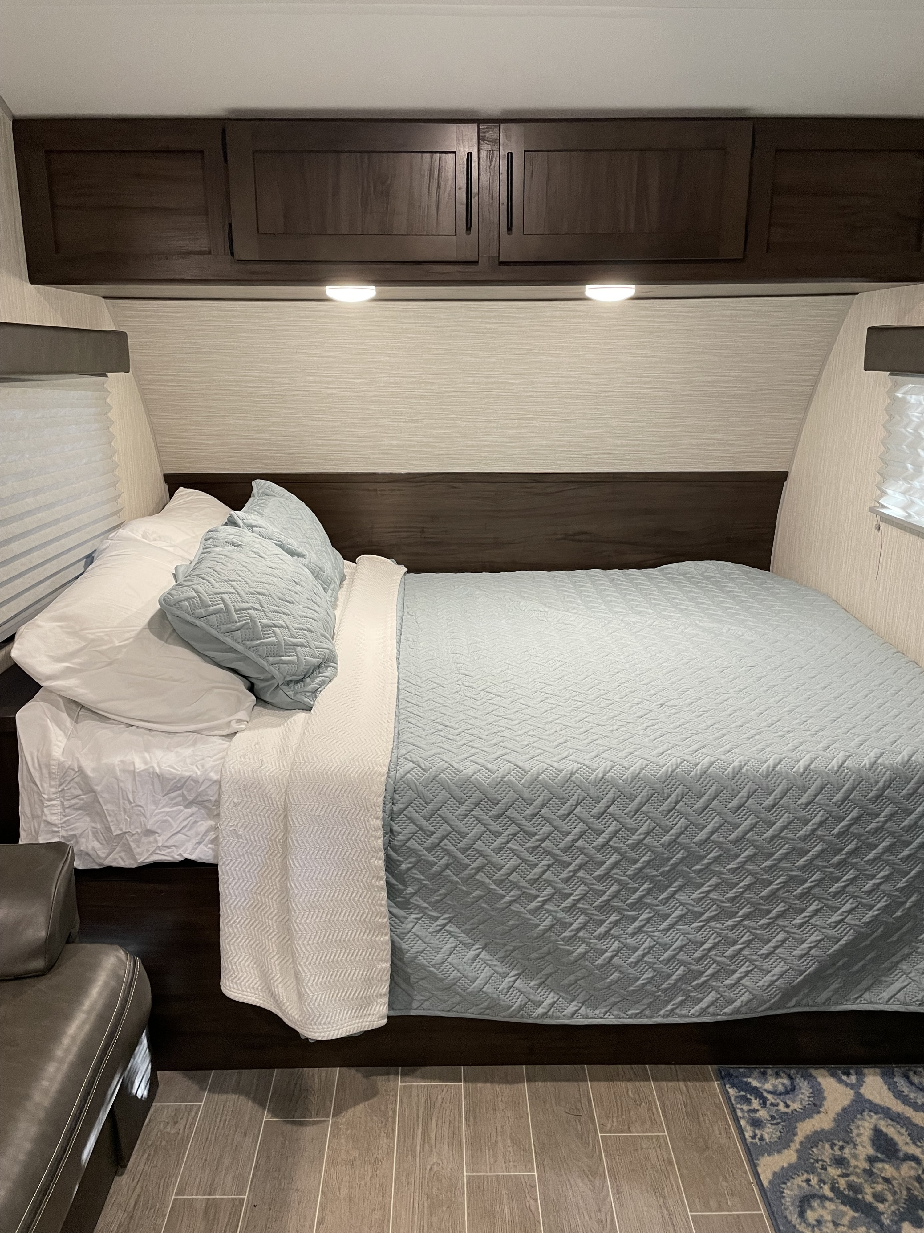 Cozy RV rental bedroom featuring a comfortable bed with light blue and white bedding, overhead storage, and wood-look flooring.. Forest River Cherokee Wolf Pup 2021