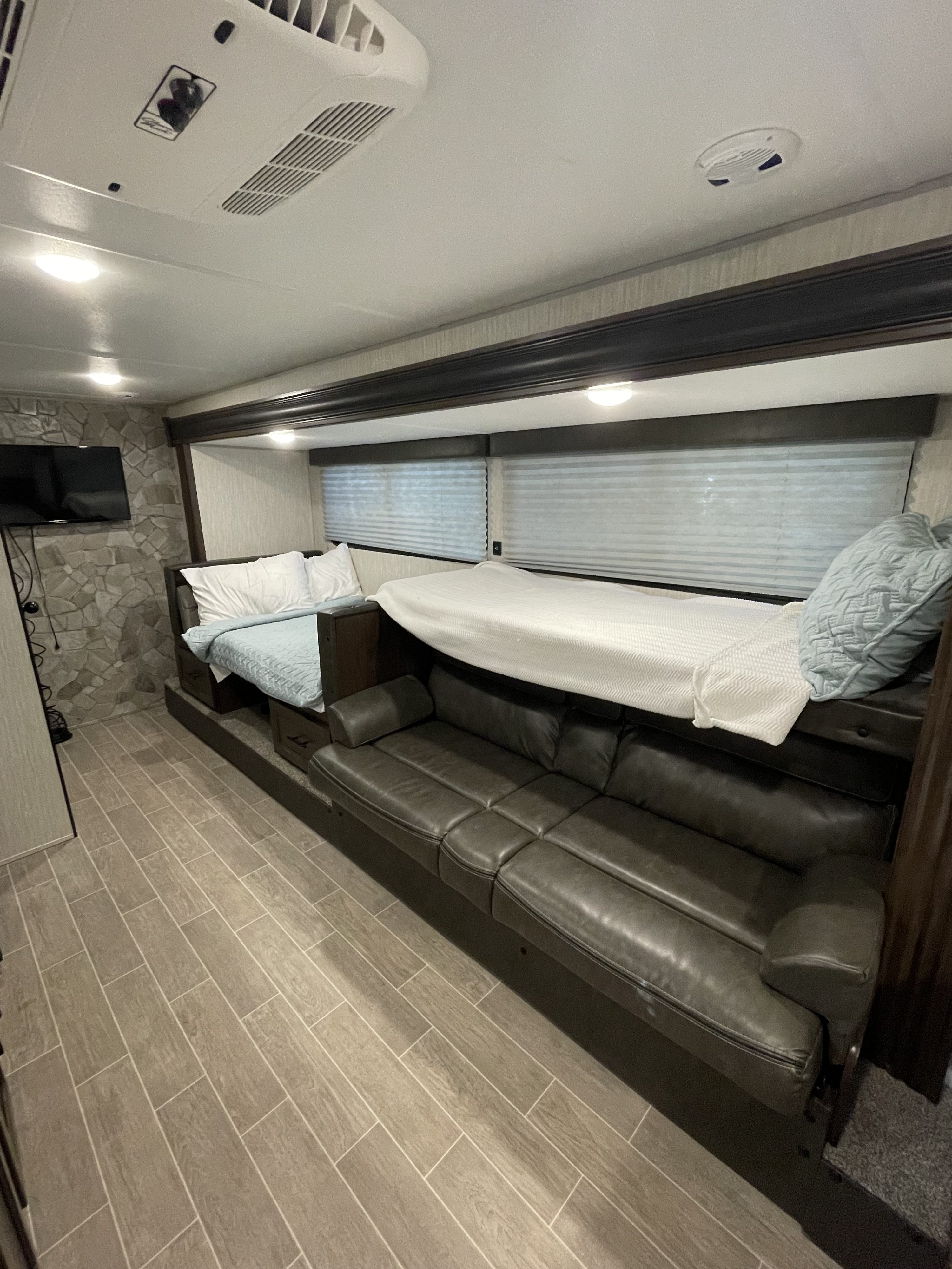 Spacious RV rental interior with comfortable bunk beds over a sofa, a wall-mounted TV, and light wood-look tile flooring.. Forest River Cherokee Wolf Pup 2021