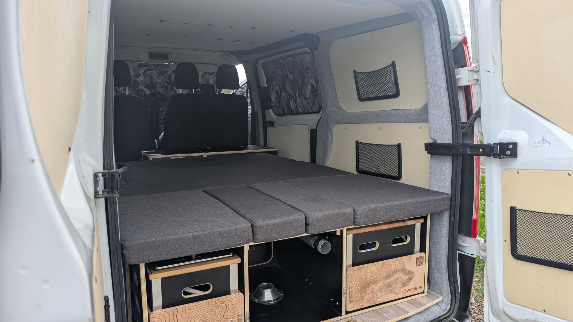 RV rental ready: A van's cozy interior with modular bed, under-bed storage, wood panels, and mesh pockets for mobile living.. Ford Transit Custom 2022