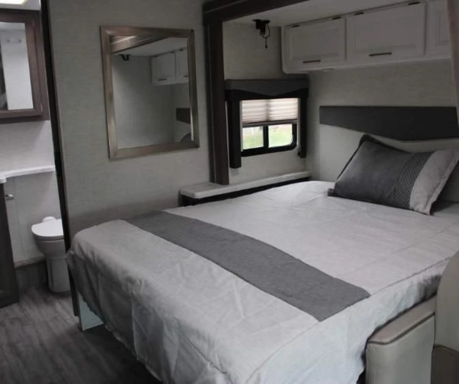 RV rental: A cozy, modern bedroom with a bed, window, and storage. The compact bathroom is visible left. Ideal for travel.. Thor Motor Coach Four Winds 2024