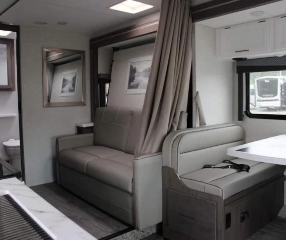 RV rental living space: a comfortable sofa that doubles as a bed, dining booth, and glimpse of the compact bathroom.. Thor Motor Coach Four Winds 2024