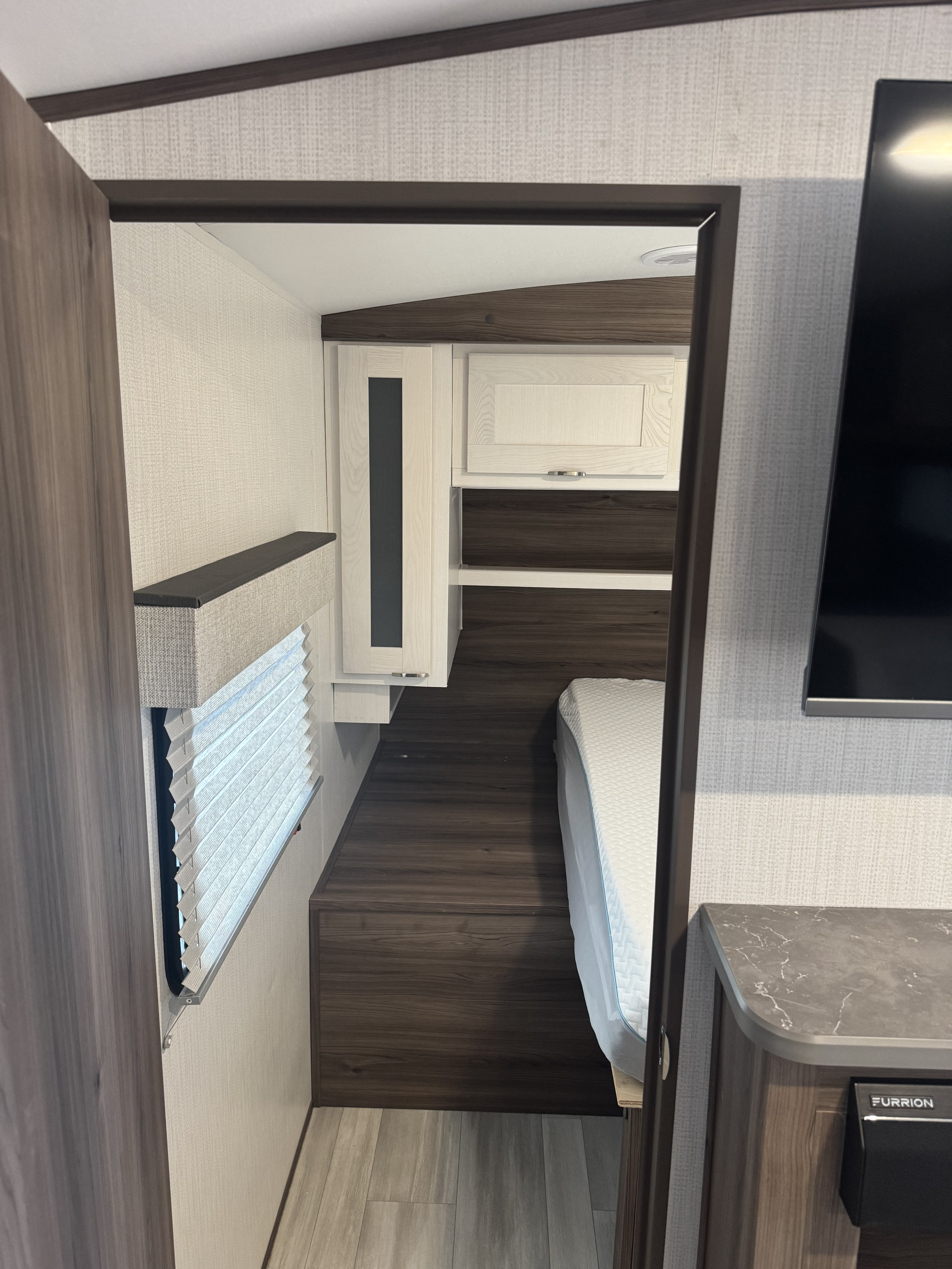 Compact RV rental bedroom featuring a bed, window with blinds, modern wood cabinetry, and wall-mounted TV.. Cruiser RV MPG 2500BH 2024