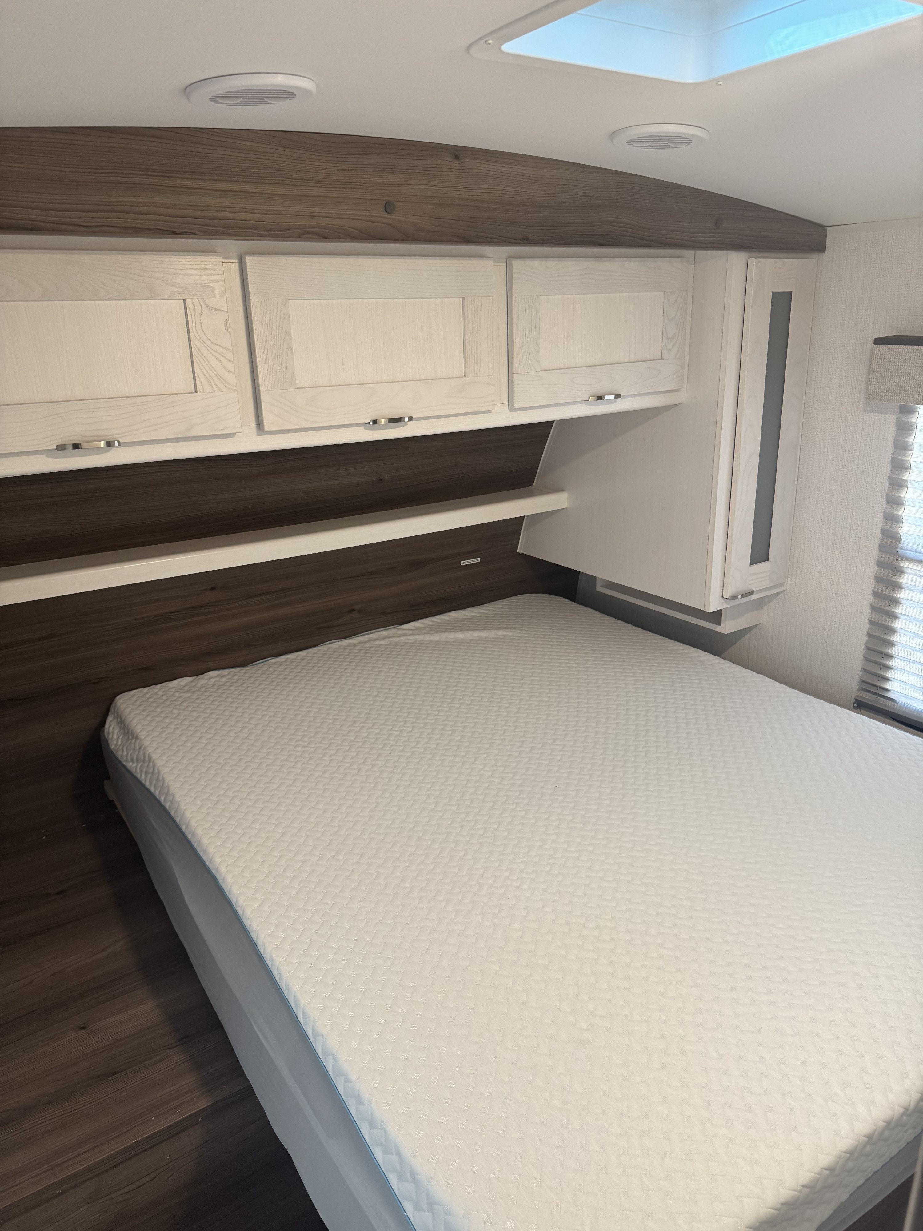 RV rental bedroom: light wood cabinets over a clean bed with dark wood accent wall & useful shelf, plus ceiling vents & skylight.. Cruiser RV MPG 2500BH 2024