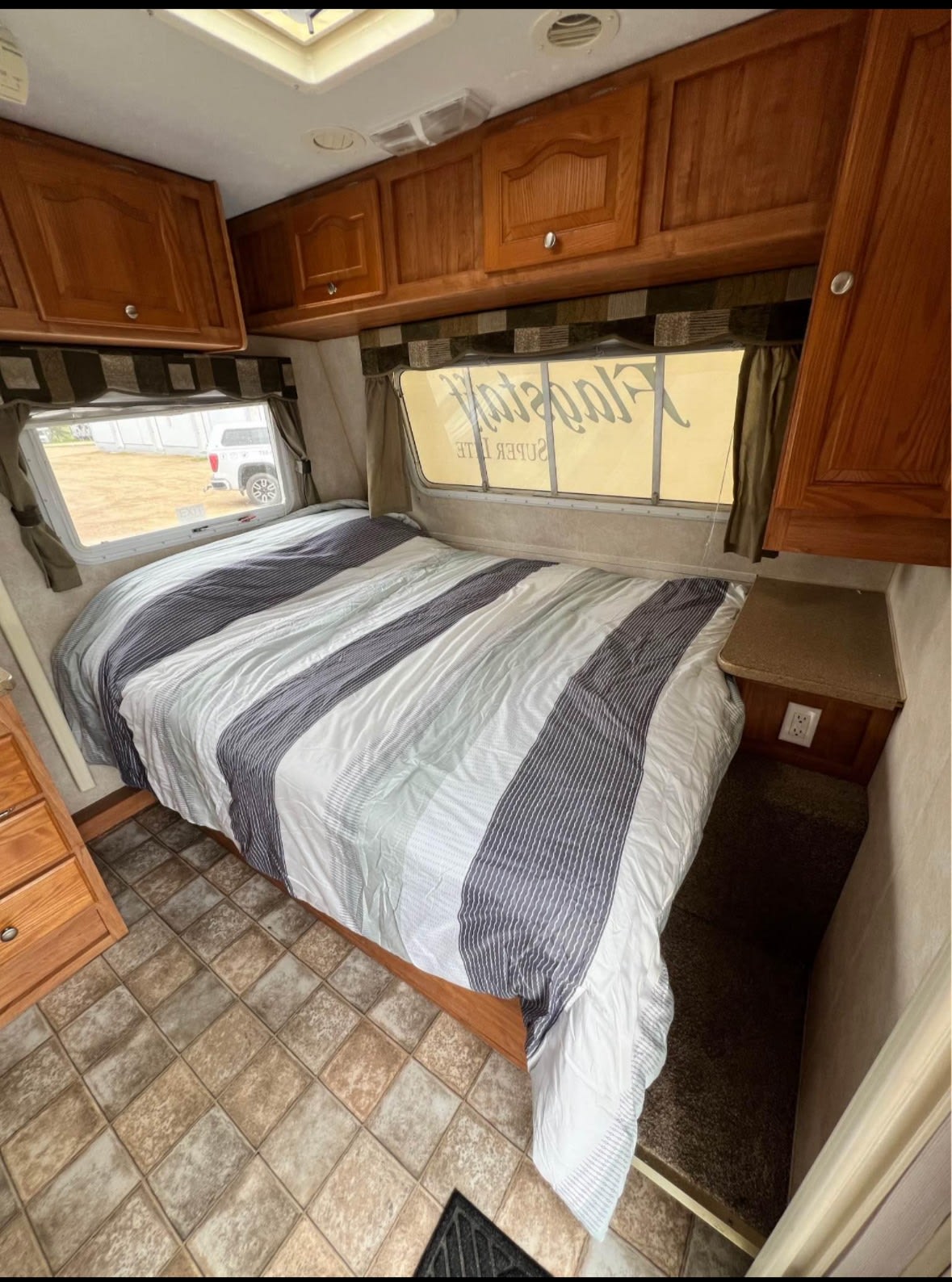 RV rental bedroom with a comfy striped bed, wooden cabinets, and large windows. The floor transitions from tile to soft carpet.. Flagstaff Super Lite 2008