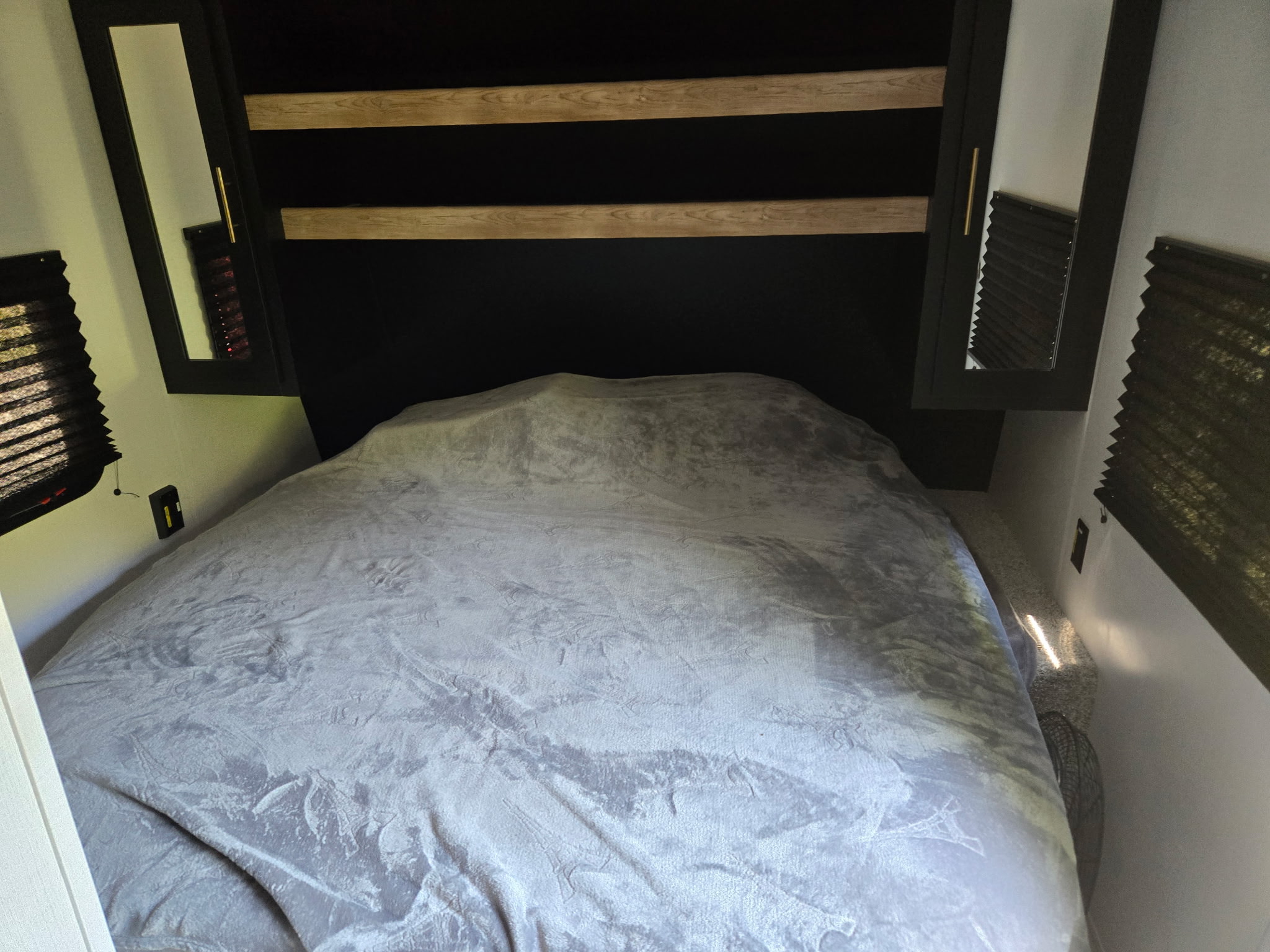 A compact RV rental bedroom is shown, featuring a soft grey bed, dark headboard, and mirrored storage.. Keystone RV Springdale 2023
