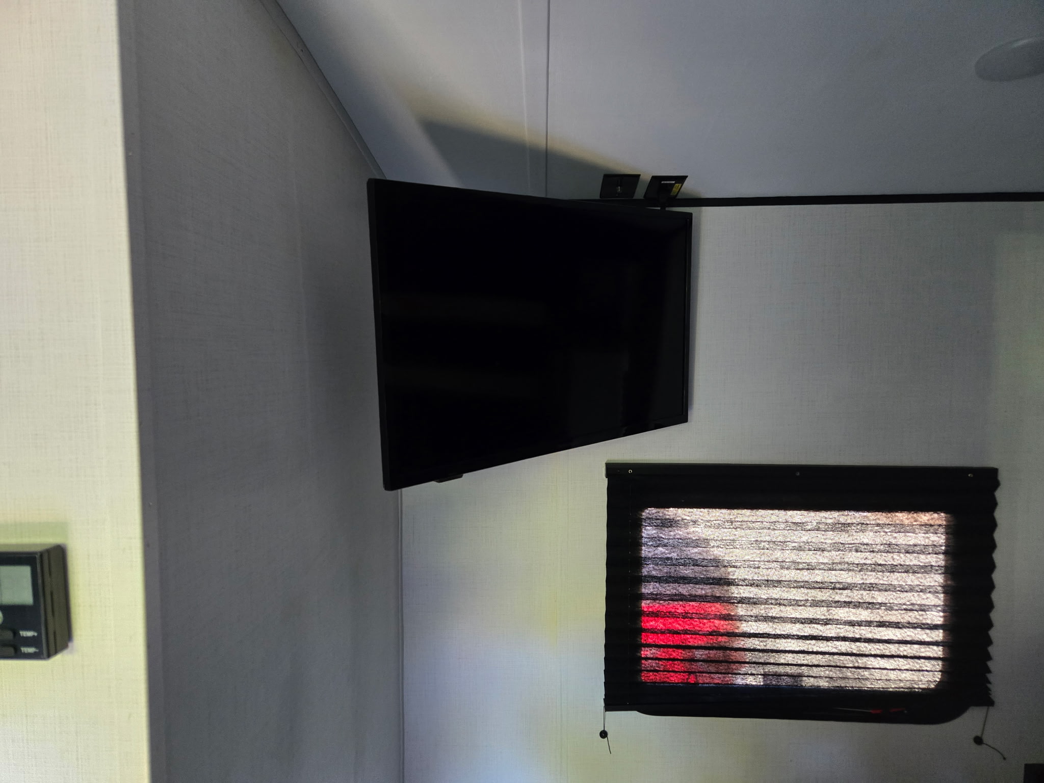 Compact RV rental interior featuring a corner-mounted TV, window with horizontal blinds, and a digital thermostat.. Keystone RV Springdale 2023