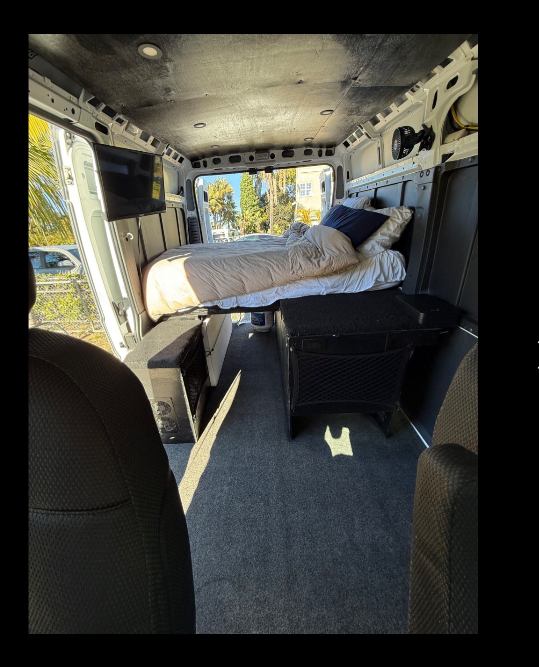 Explore this RV rental's comfy camper van interior, complete with a bed, wall-mounted TV, and organized storage.. Ram Promaster 2022
