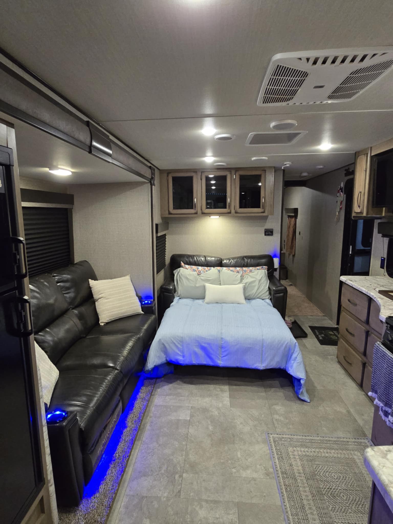 Cozy RV rental interior with black leather sofa, pull-out bed with blue accent lighting, and compact kitchen space.. Grand Design Transcend 2019