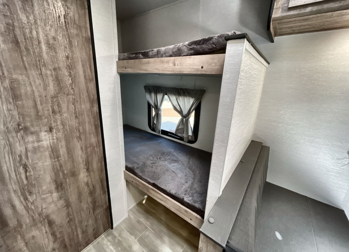 Cozy RV rental interior featuring stacked bunk beds with gray bedding and window, ideal for family trips.. Gulf Stream Enlighten 2025