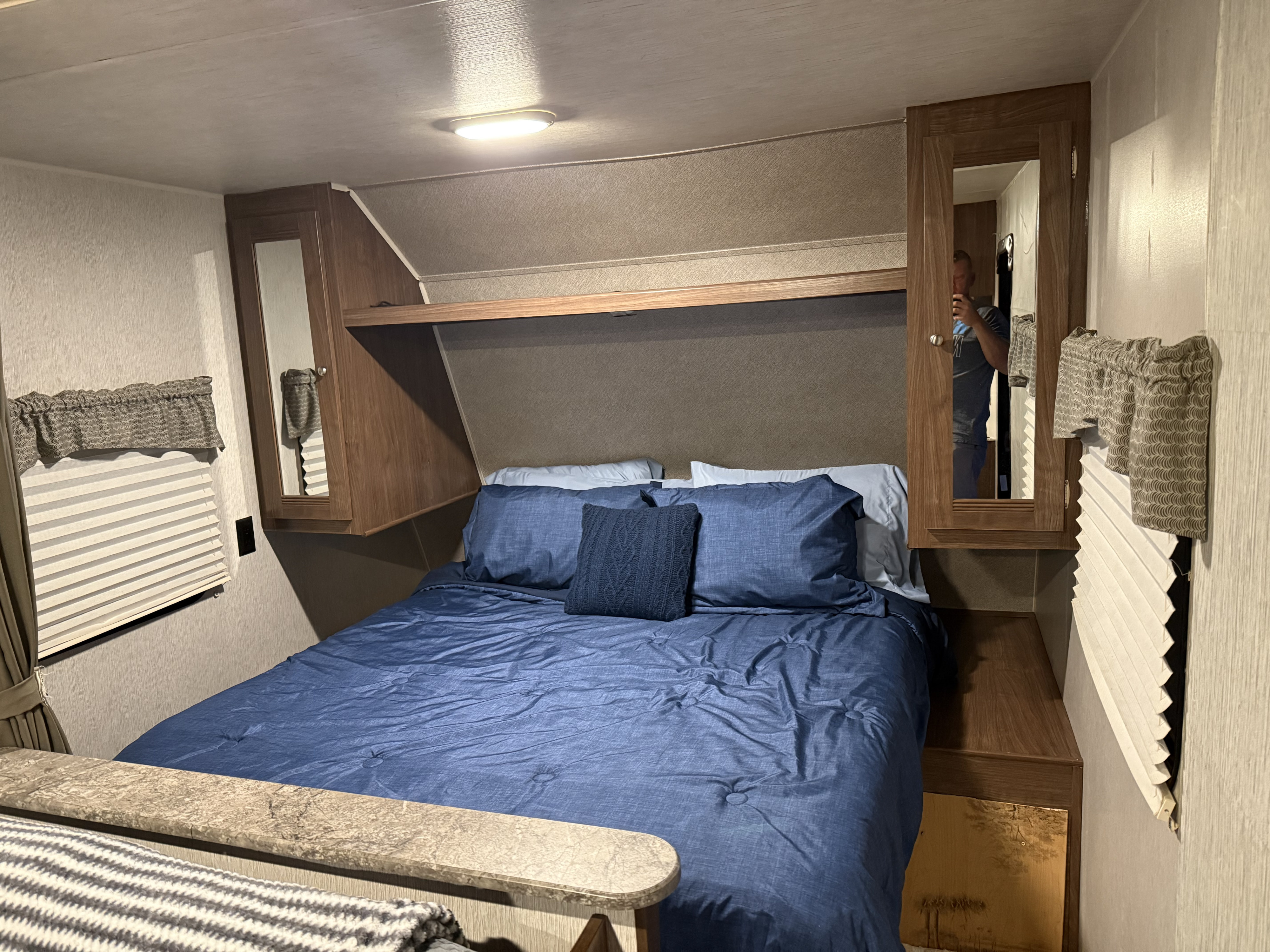 Cozy RV rental bedroom with blue bedding, overhead storage, and window blinds, providing a comfortable space for travel.. Heartland RVs Trail Runner SLE 2018