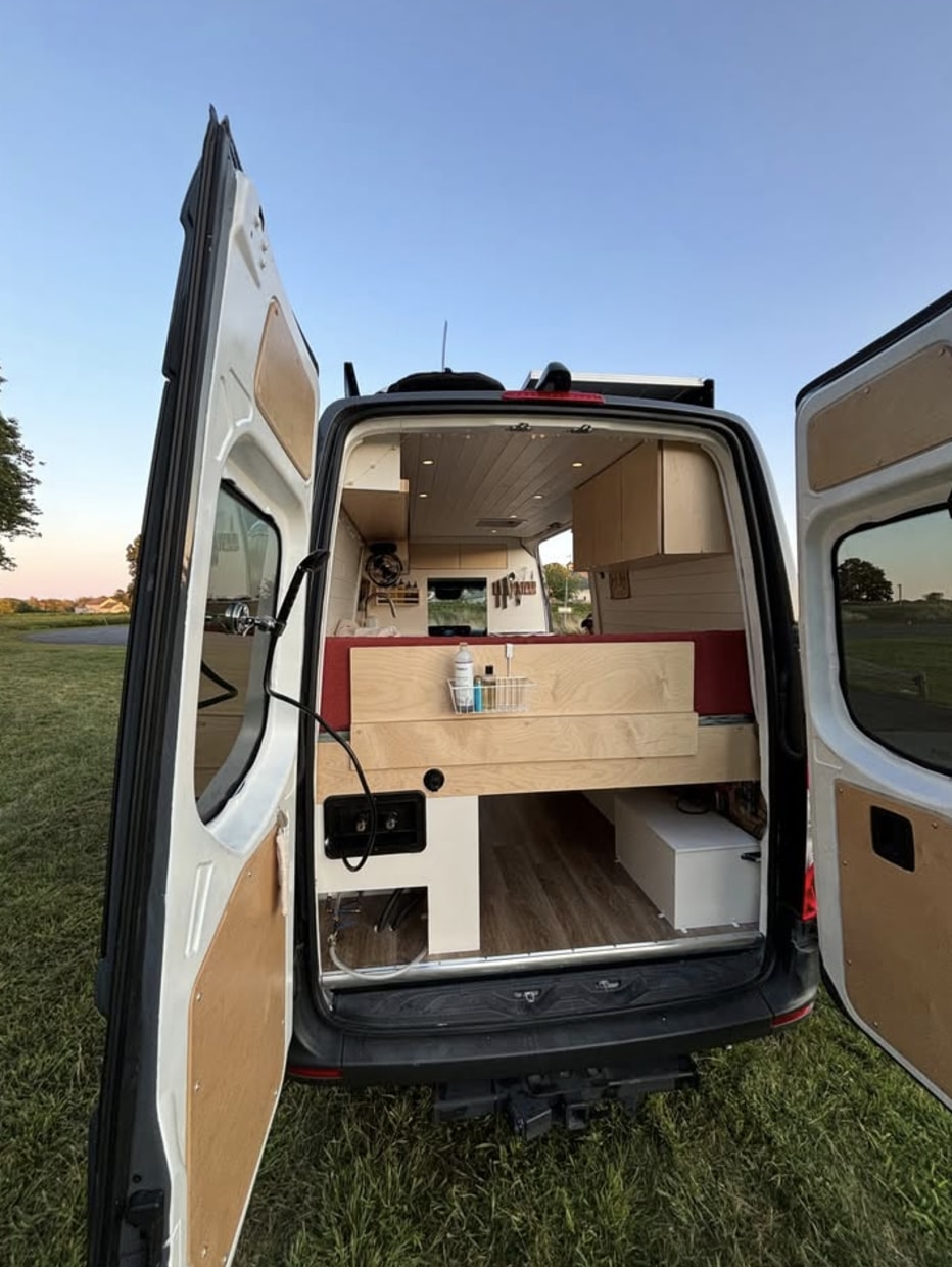 Explore this custom camper van's interior, perfect for your next rv rental. Shows bed, storage, and utility setup from the rear.. Mercedes Benz Sprinter 144 Diesel 2023