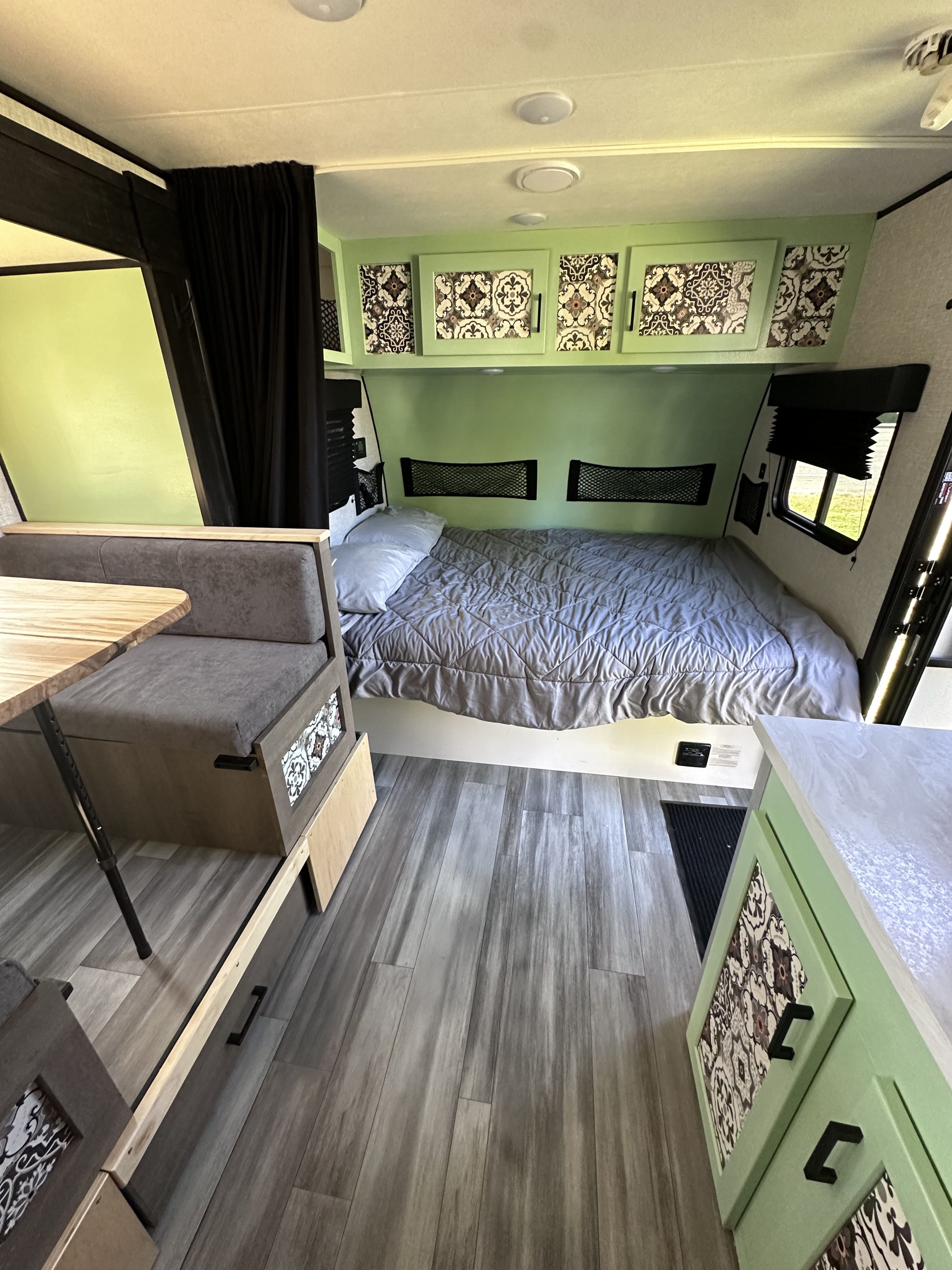 Inside an RV rental: a comfortable bed, dinette, and light green cabinets with patterned fronts.. Jayco Jayflight BAJA 2024